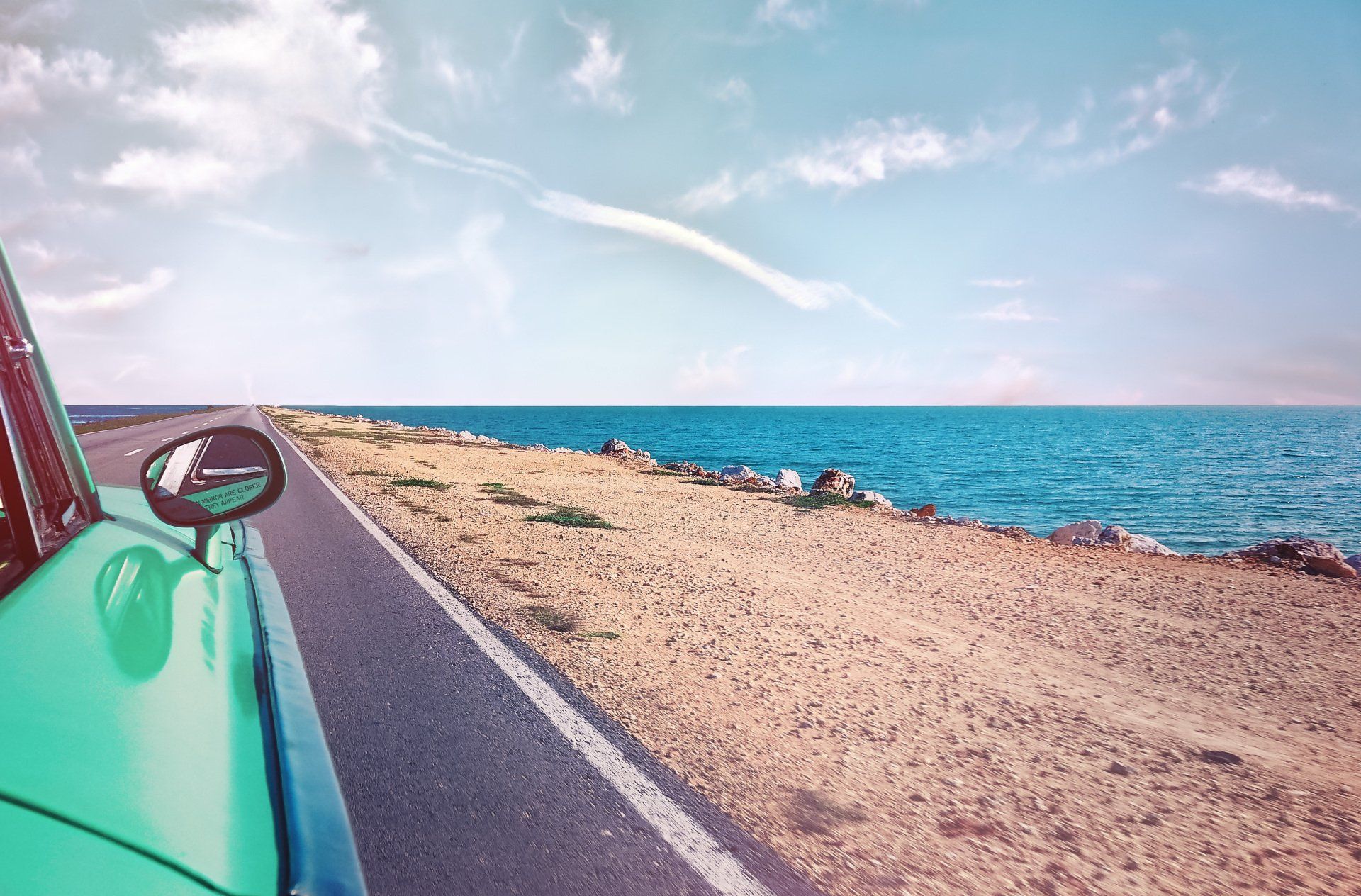 A car is driving down a road next to the ocean.