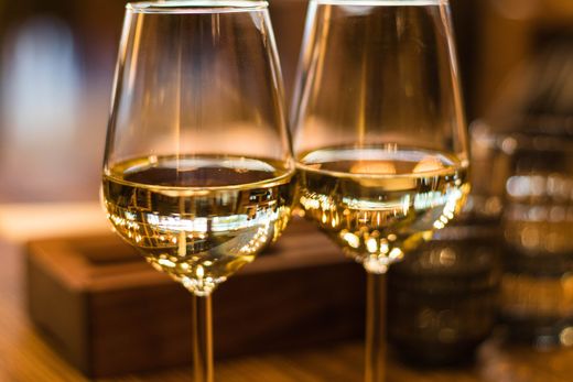 Two glasses of white wine on a wooden table, softly lit in a warm setting