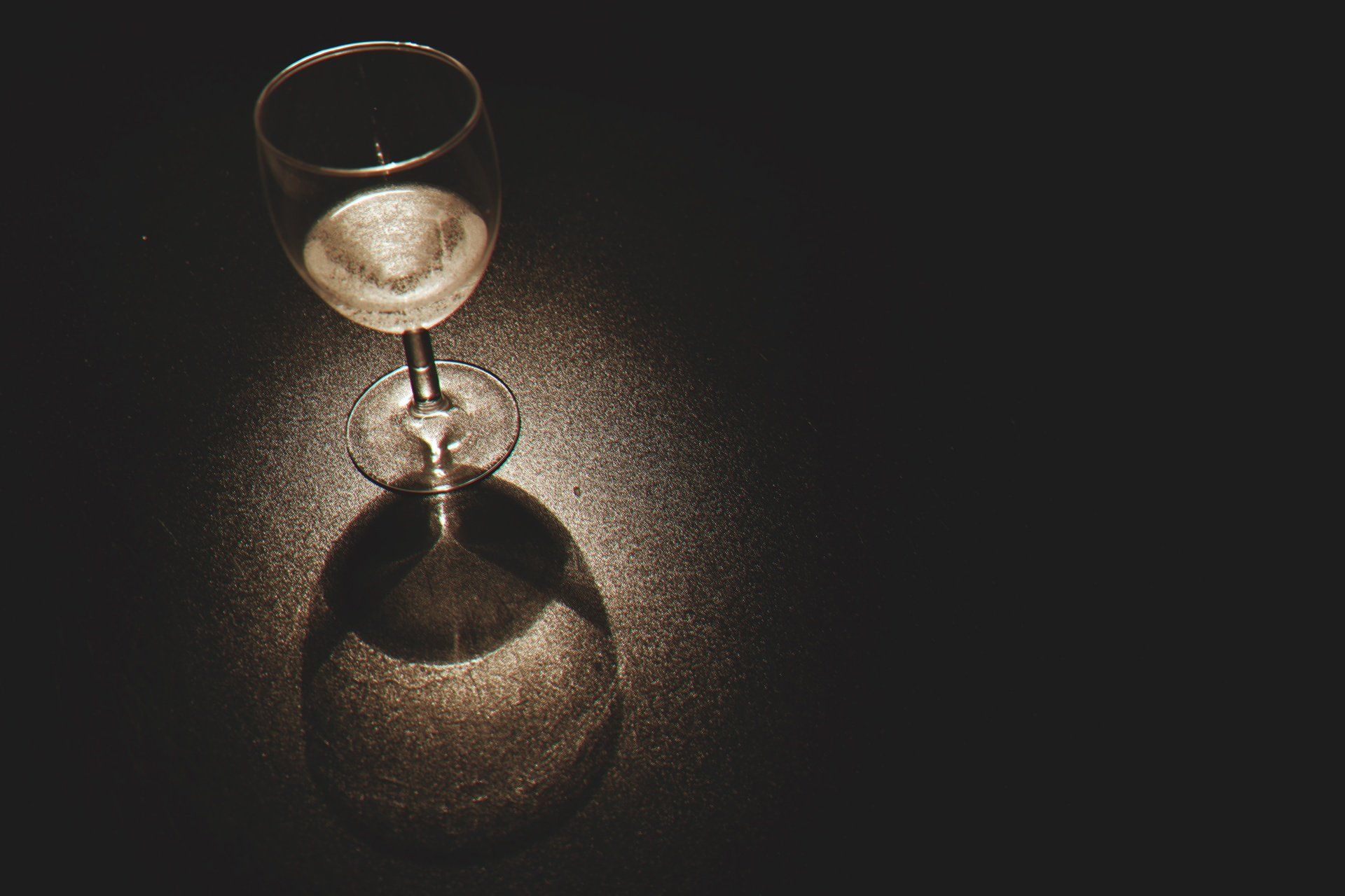 A wine glass is sitting on a table in the dark.