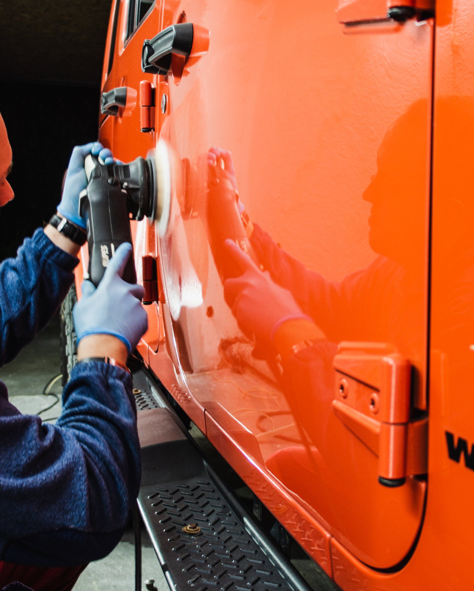 a man is polishing the side of an orange jeep