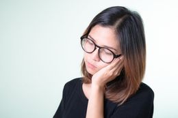 a woman wearing glasses is covering her face with her hand .