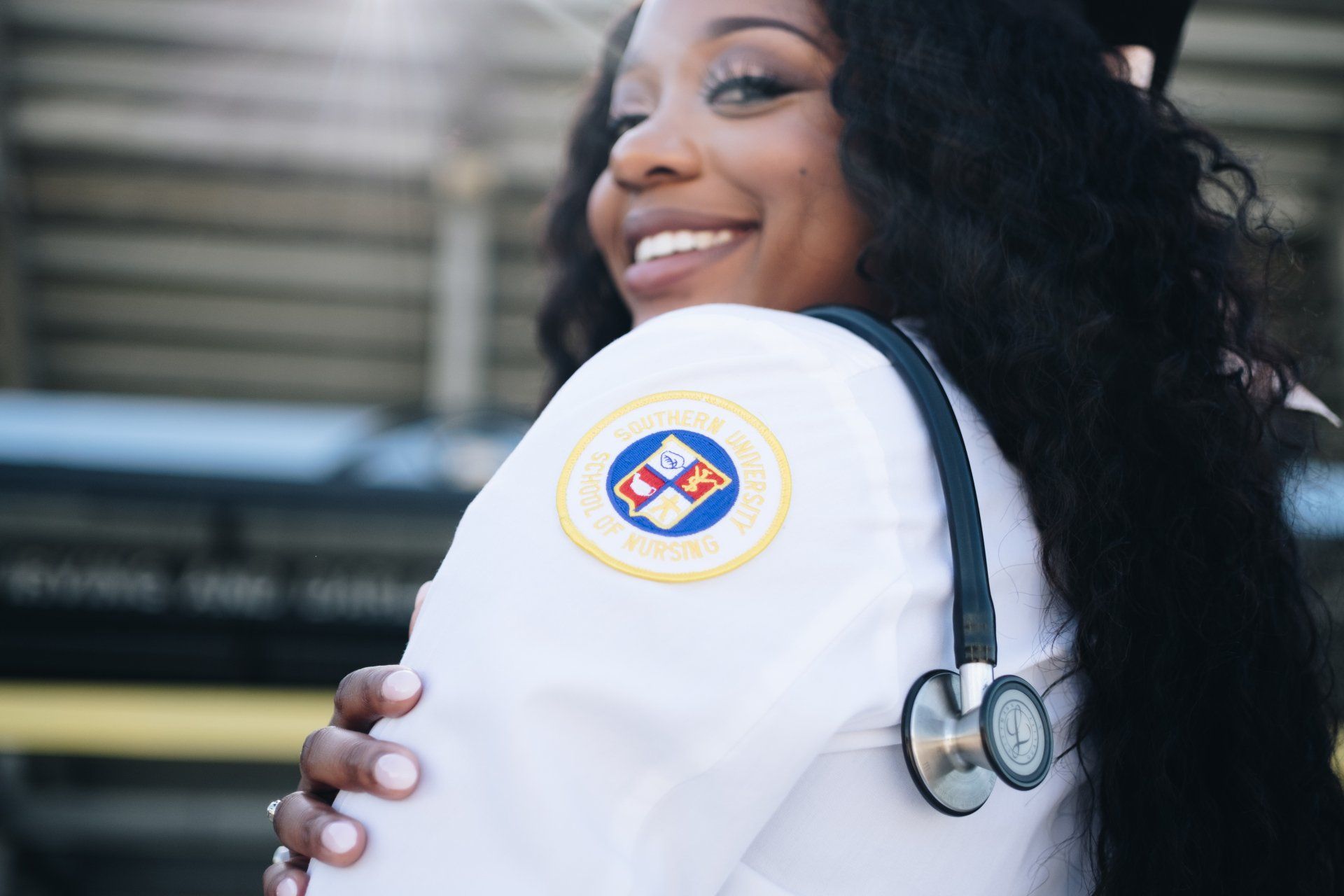 A woman in a white lab coat with a stethoscope around her neck is smiling.