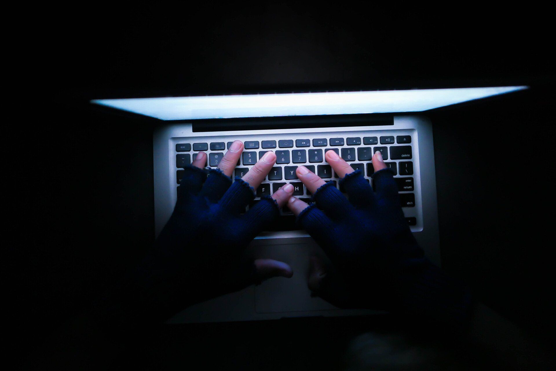 A person wearing gloves is typing on a laptop keyboard.