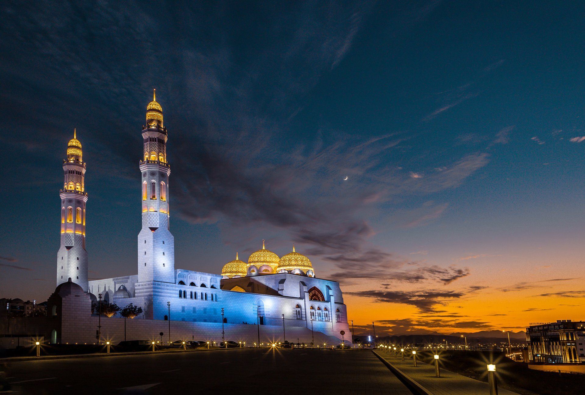 A mosque is lit up at night with a sunset in the background.