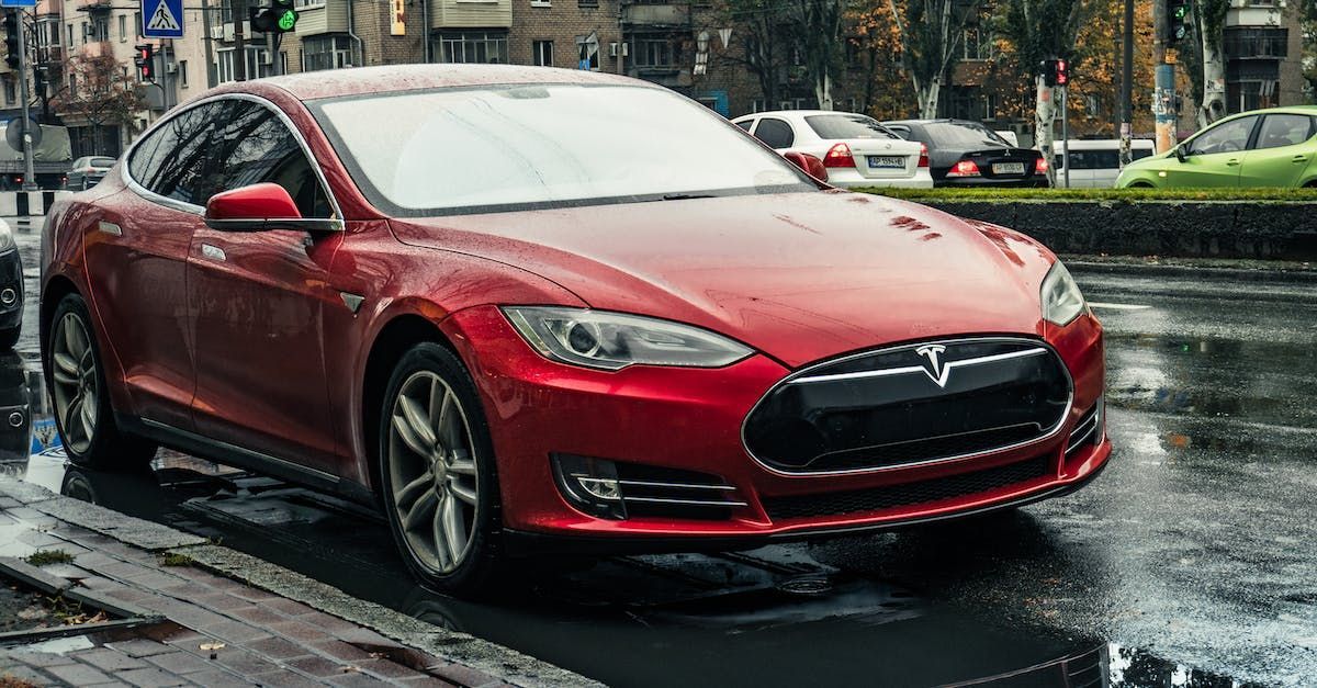 A red tesla model s is parked on the side of the road in the rain.