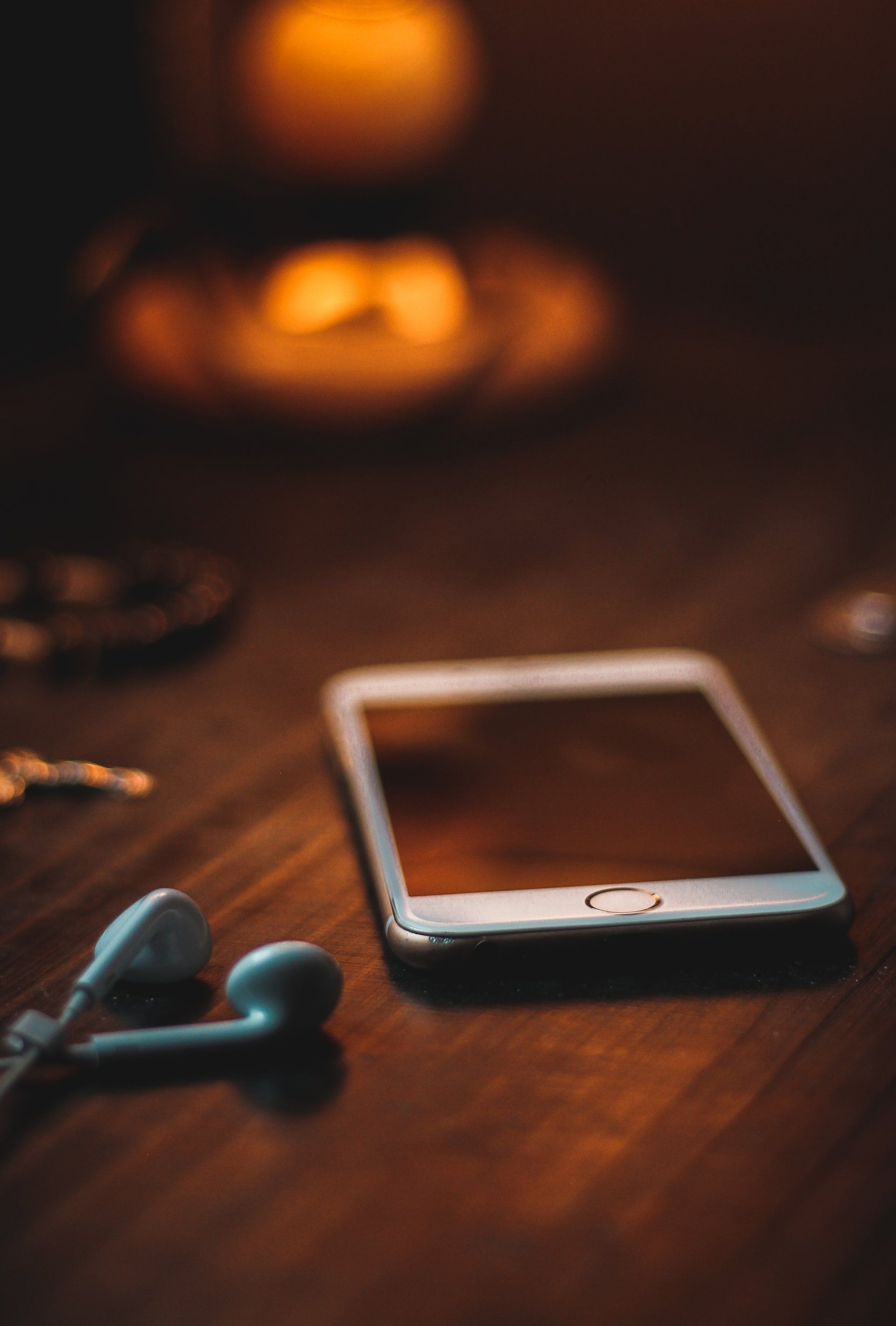 Smartphone with earbuds on a wooden surface, dimly lit with a warm glow.