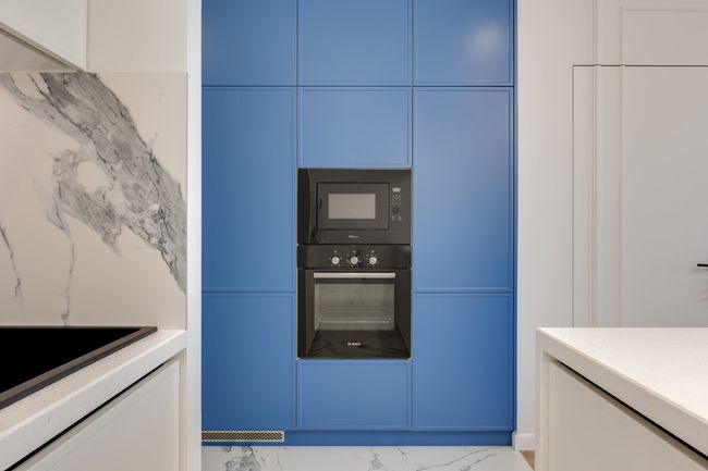 A kitchen interior with blue floor-to-ceiling cabinets, a built-in oven and microwave, and marble-patterned surfaces.
