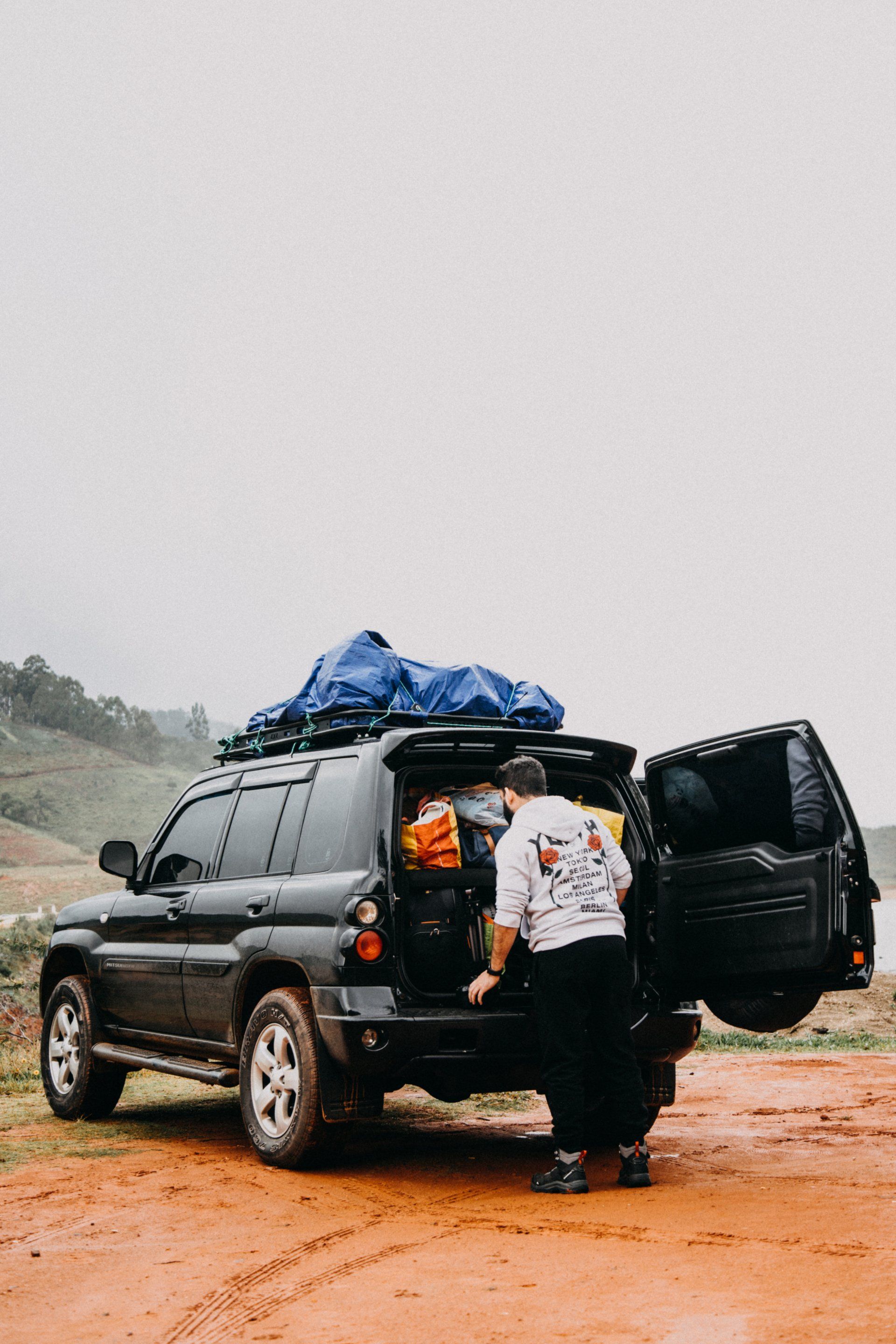 Person loading cargo into a black SUV on a muddy dirt road under a cloudy sky.