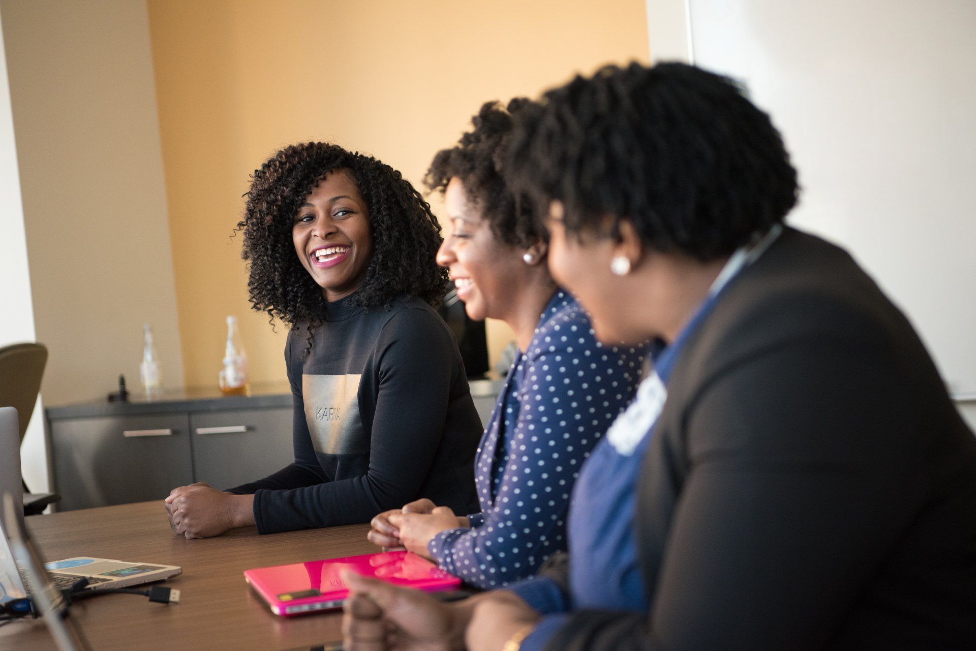 Three coworkers chatting at a conference table with laptops and notebooks