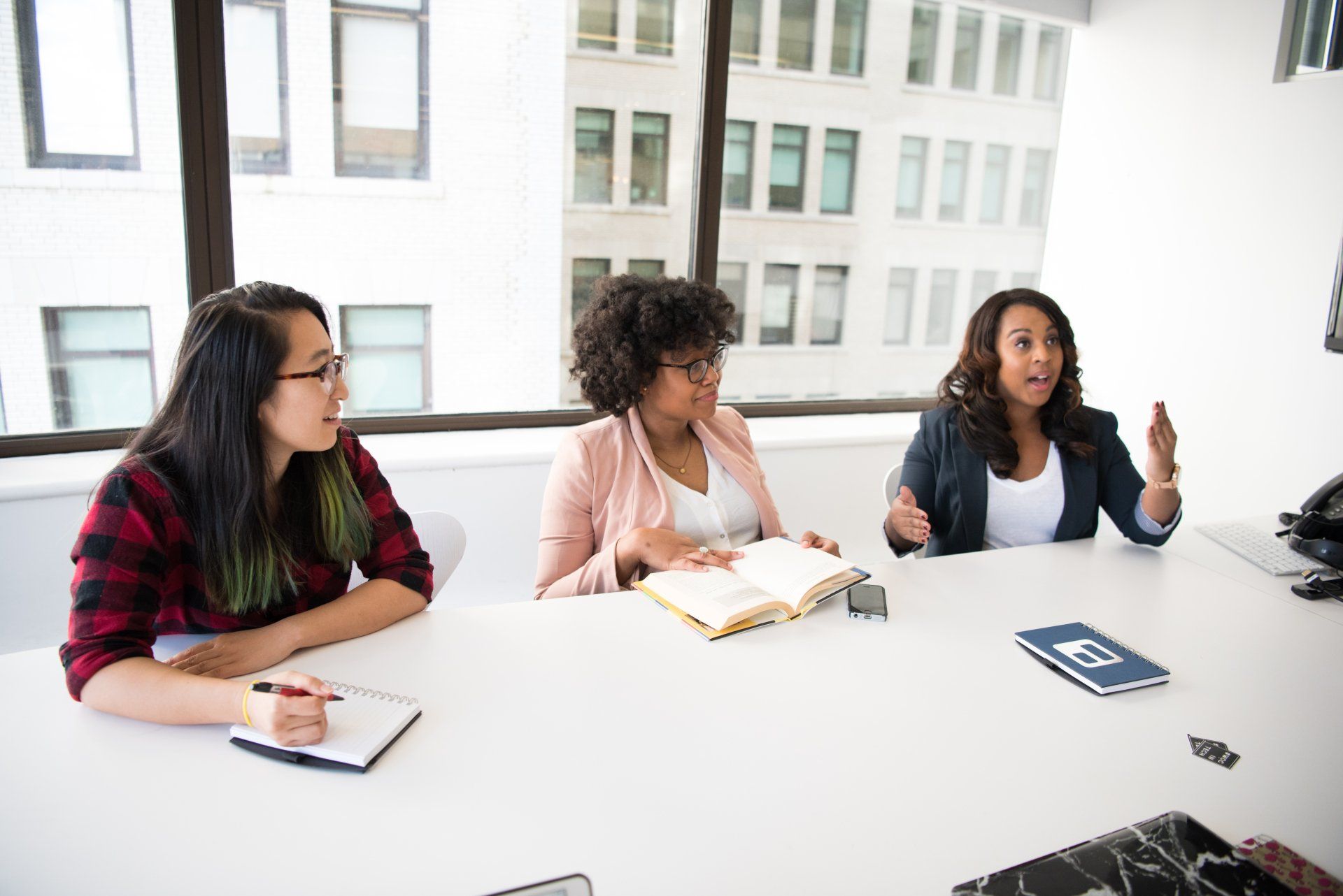 Three women are sitting at a table with a notebook that says ' ep ' on it