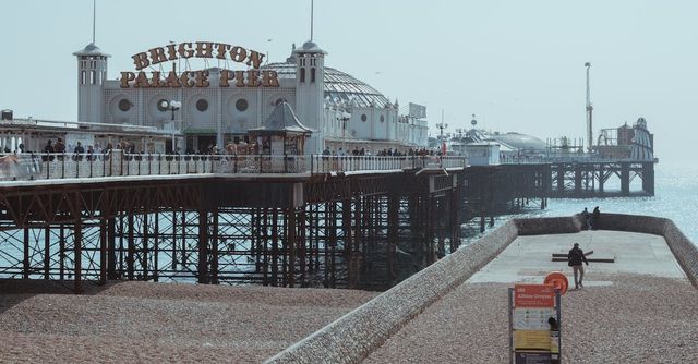 An old seaside pier with buildings on stilts over the water and a pebble beach under a gray sky