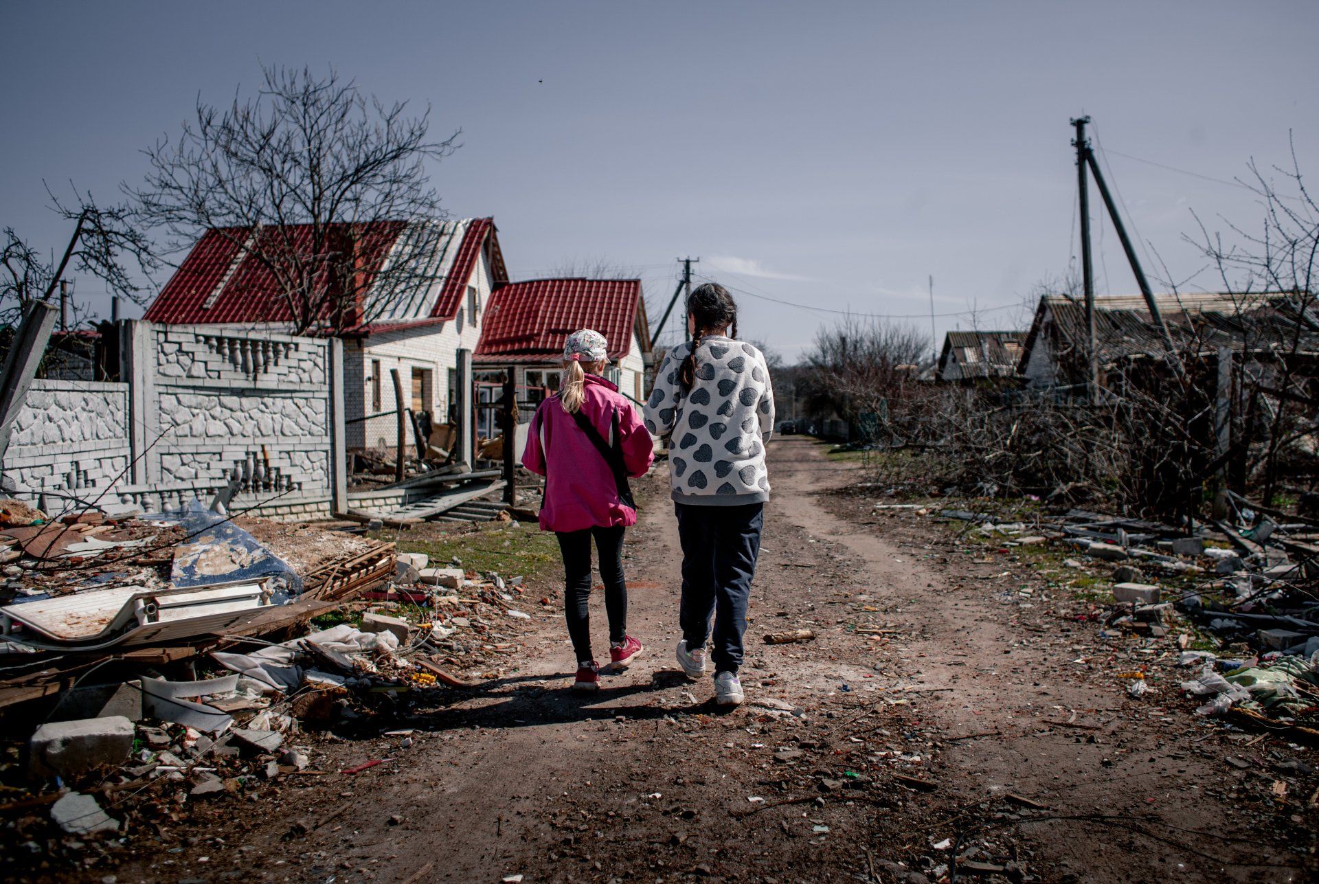 Two people walking down a dirt road with a house in the background