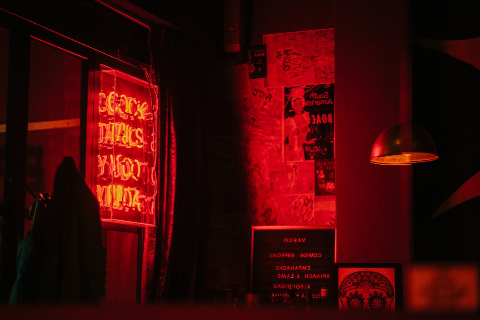 Karanlık bir barda parlak kırmızı bir neon tabela, duvarda posterler ve parlak bir aydınlatma armatürü.