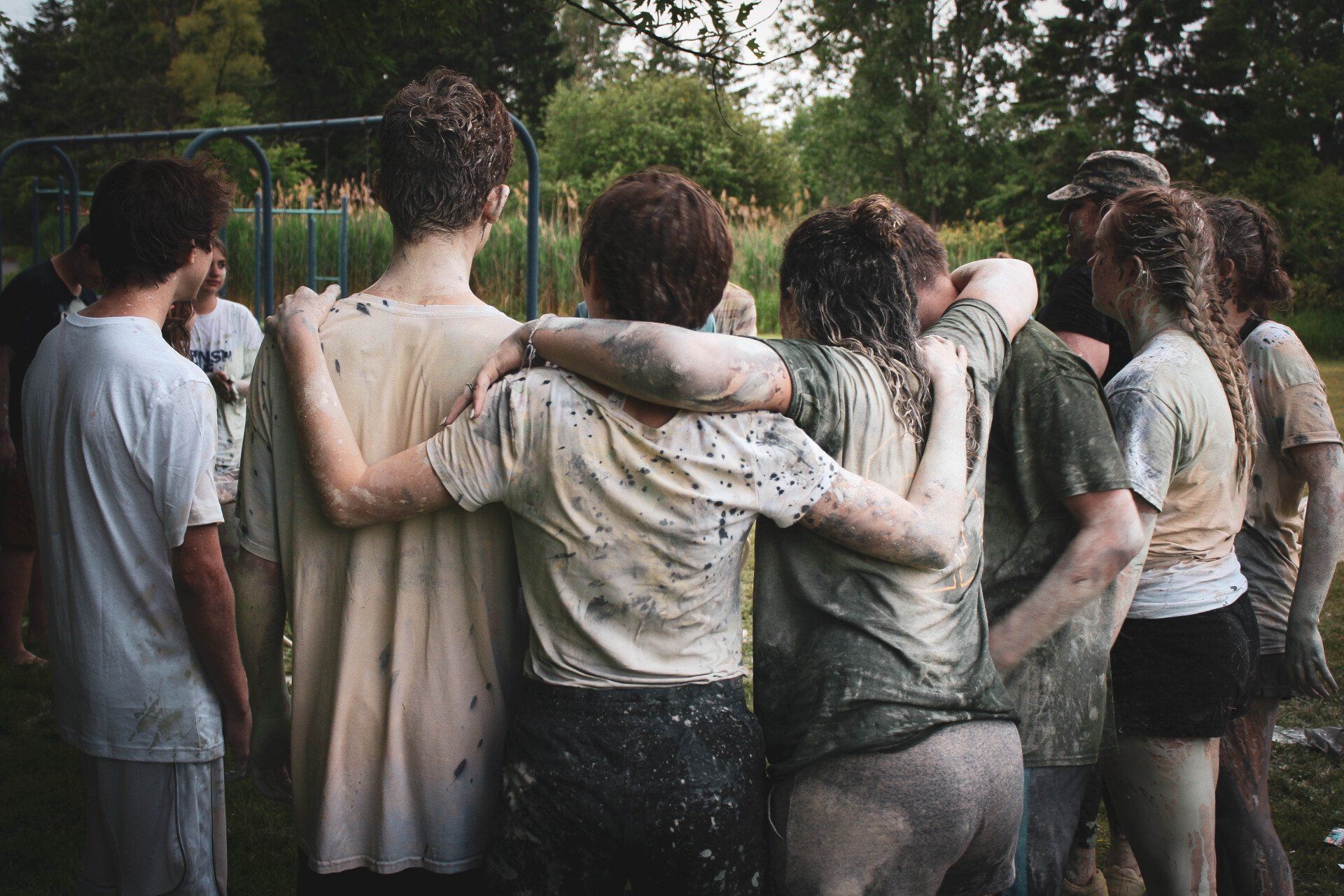Group of friends with muddy clothes, arms around each other, celebrating outdoors.