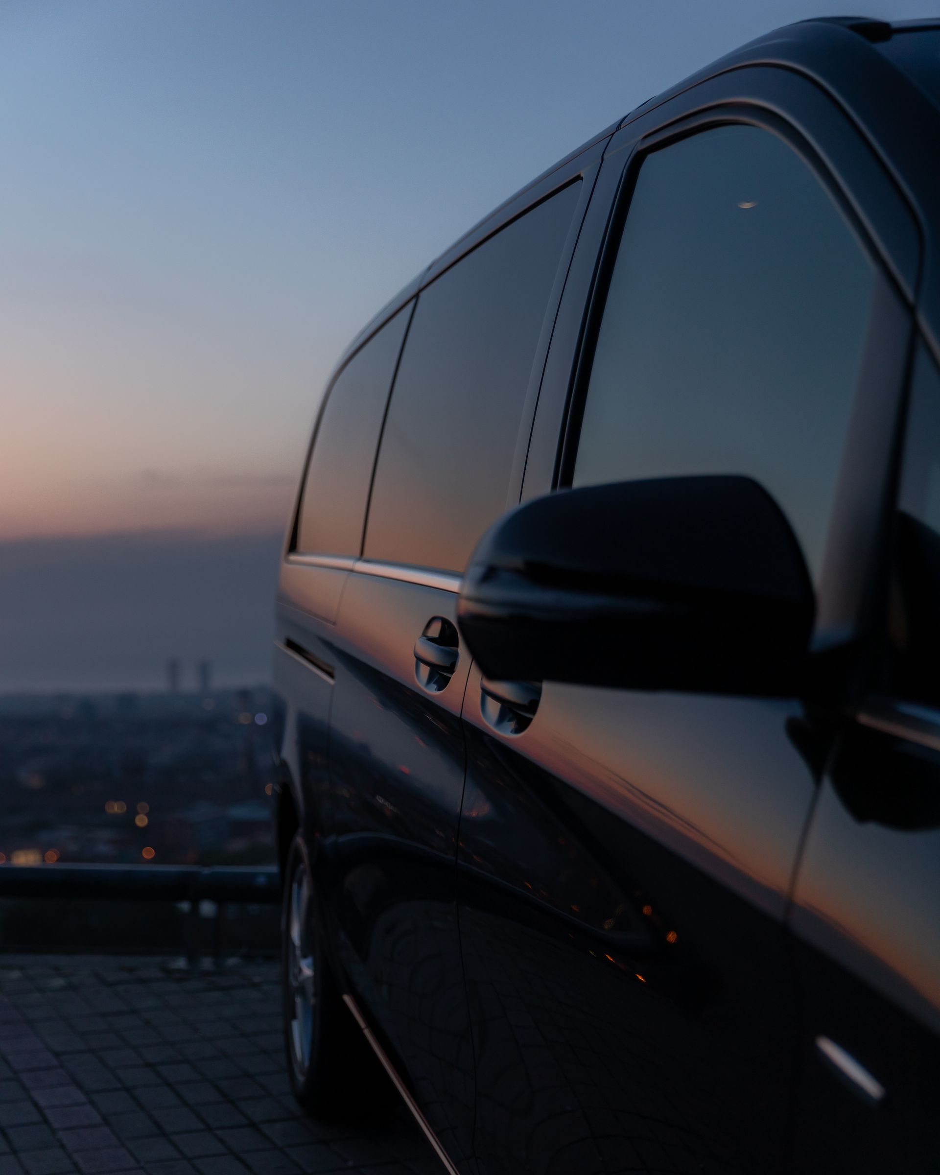 Black van parked, reflecting the twilight sky over a city.