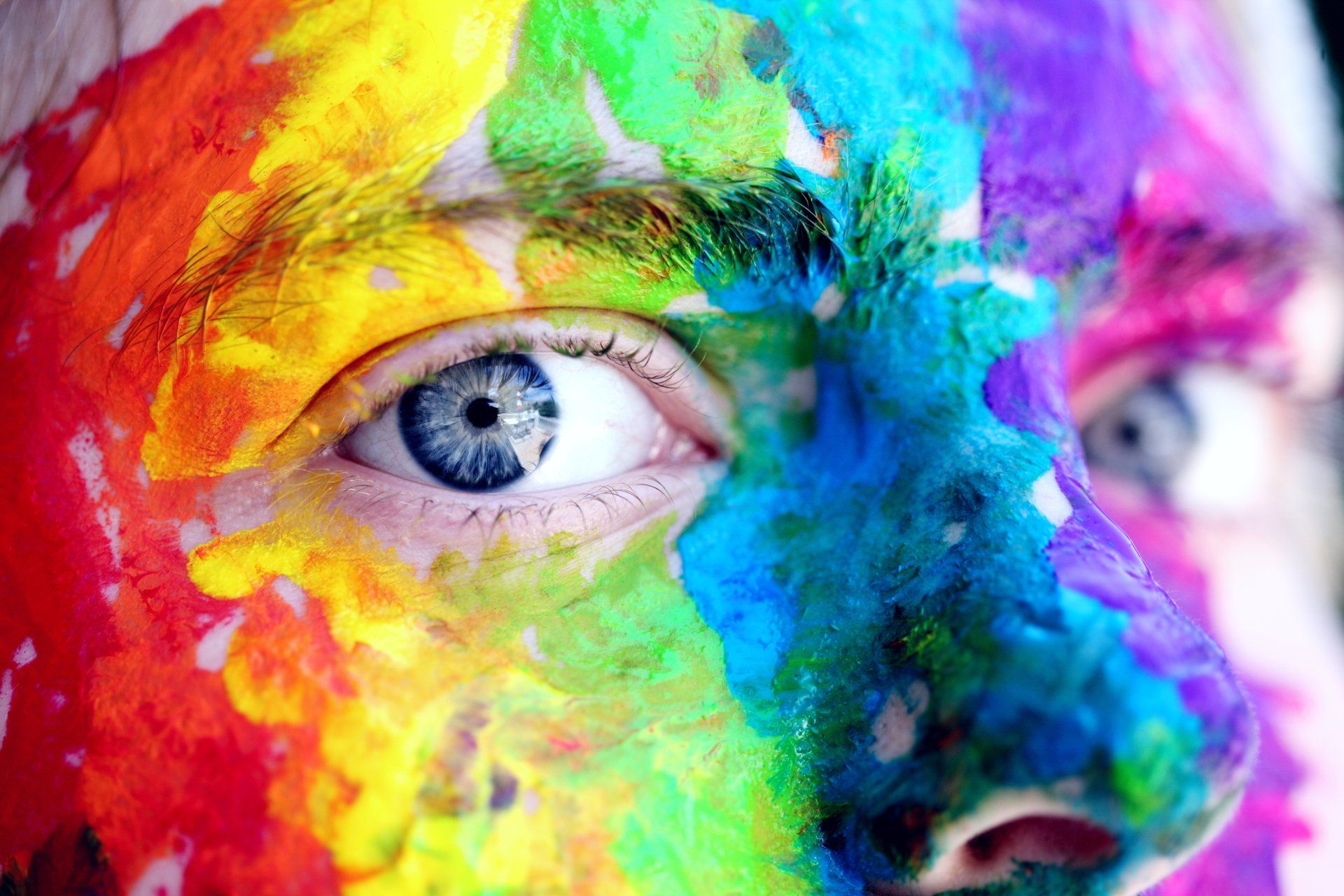 Face covered in rainbow paint, blue eye.