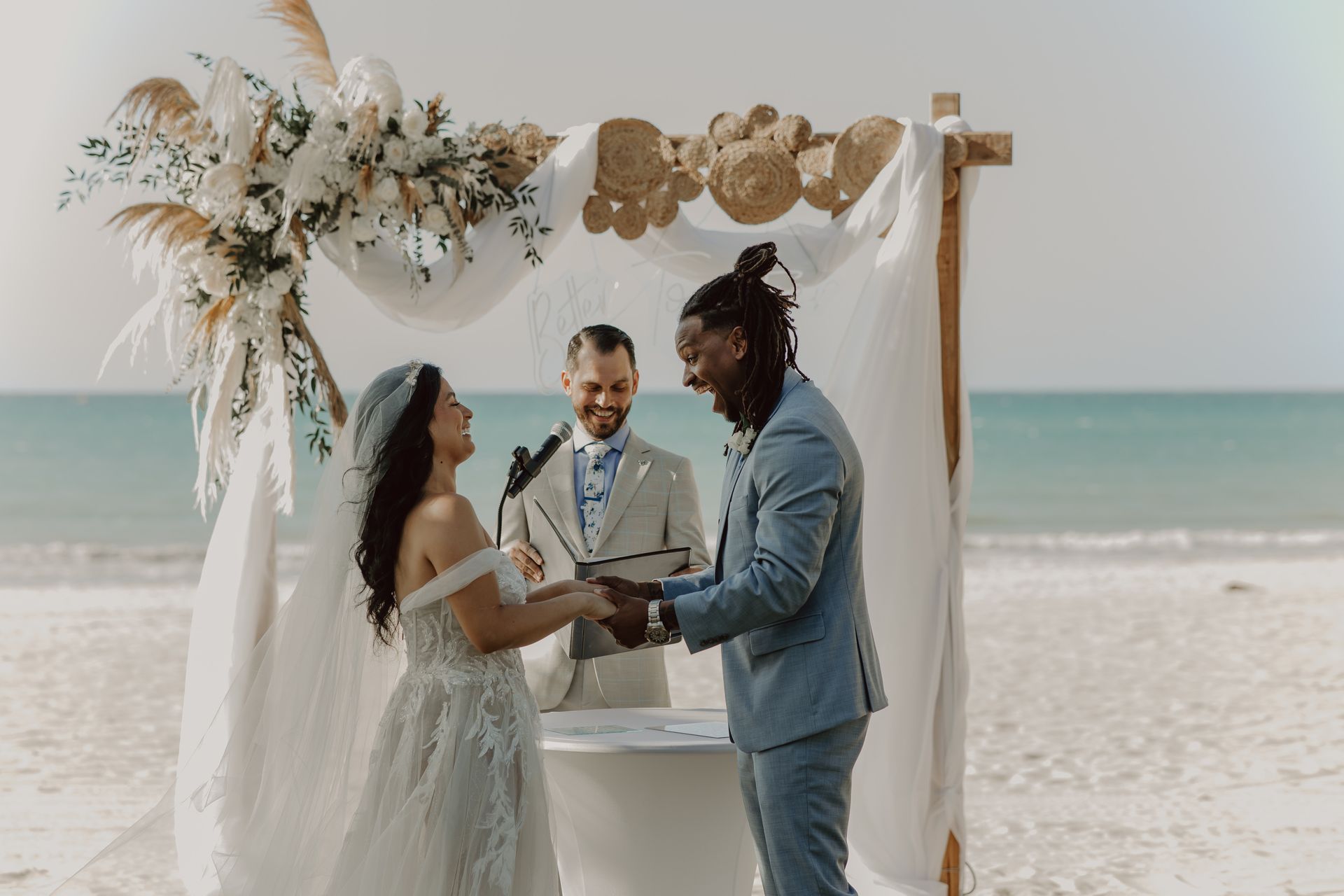 A bride and groom are holding hands during their wedding ceremony on the beach.