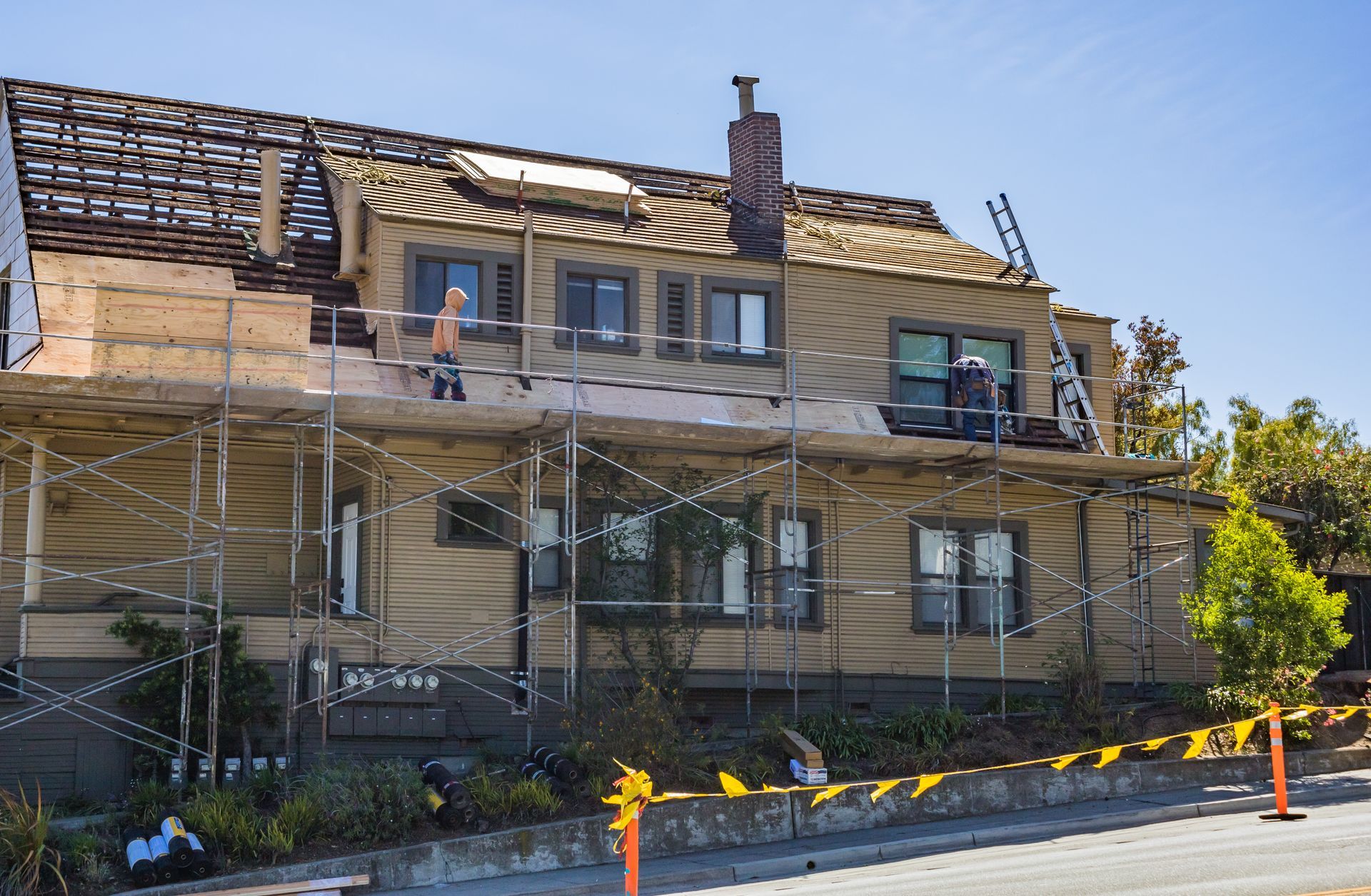 House undergoing roof repairs, scaffolding surrounding. Workers on roof.