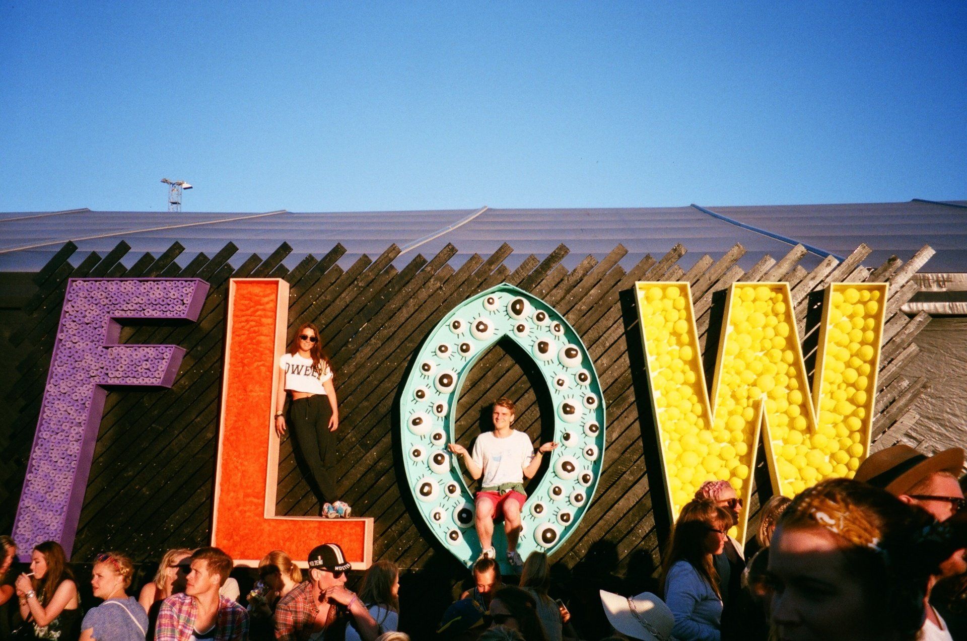 Colorful “FLOW” marquee letters with people standing and dancing in front at an outdoor event