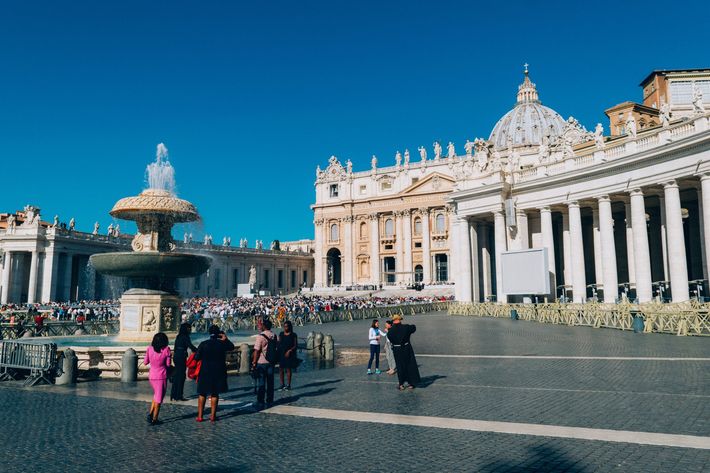 A group of people are walking around a fountain in front of a large building.