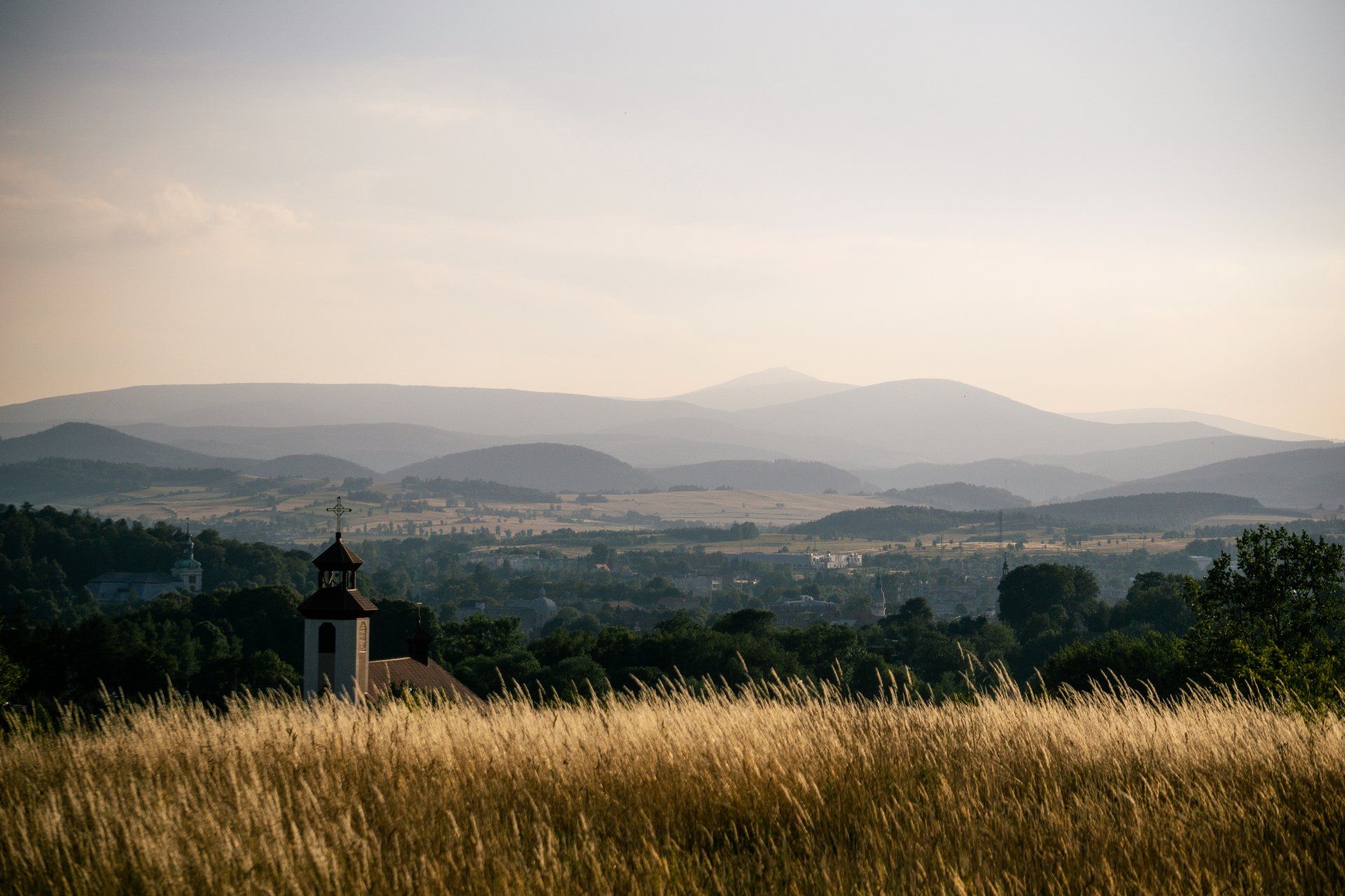 There is a church in the middle of a field with mountains in the background.