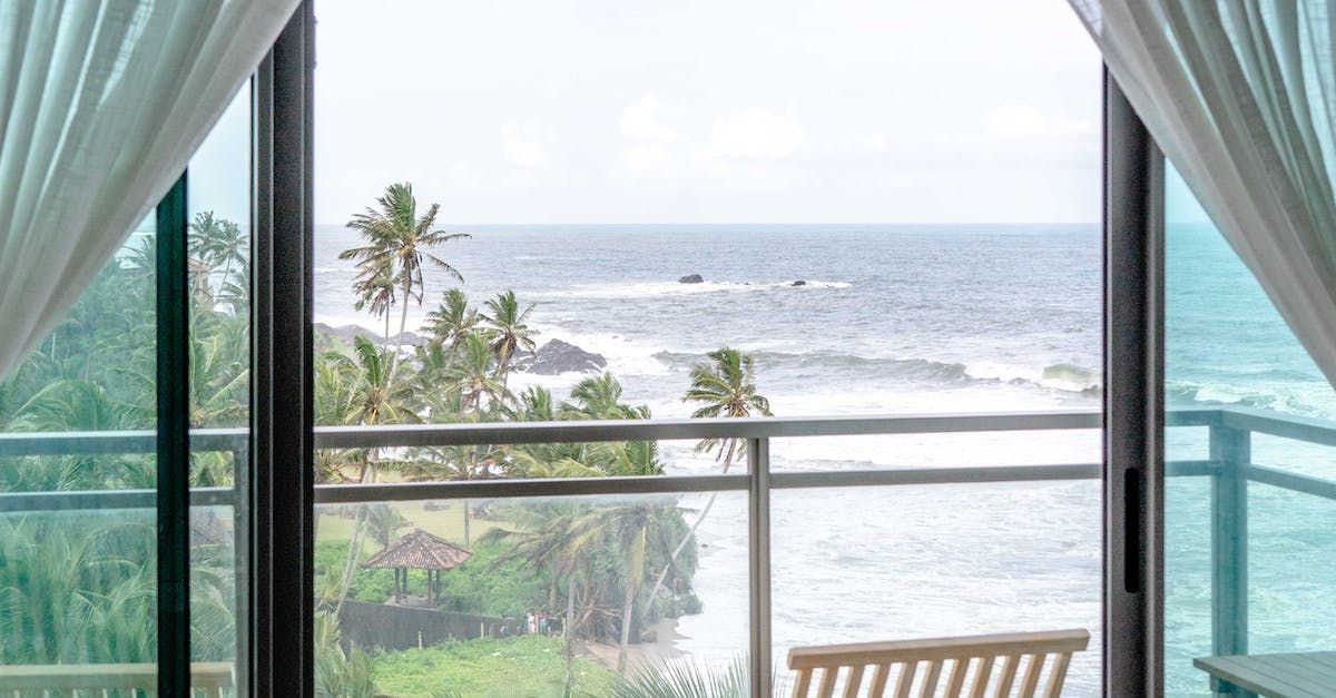 Ocean view through sliding glass doors, balcony with chair, palm trees, and white curtains.