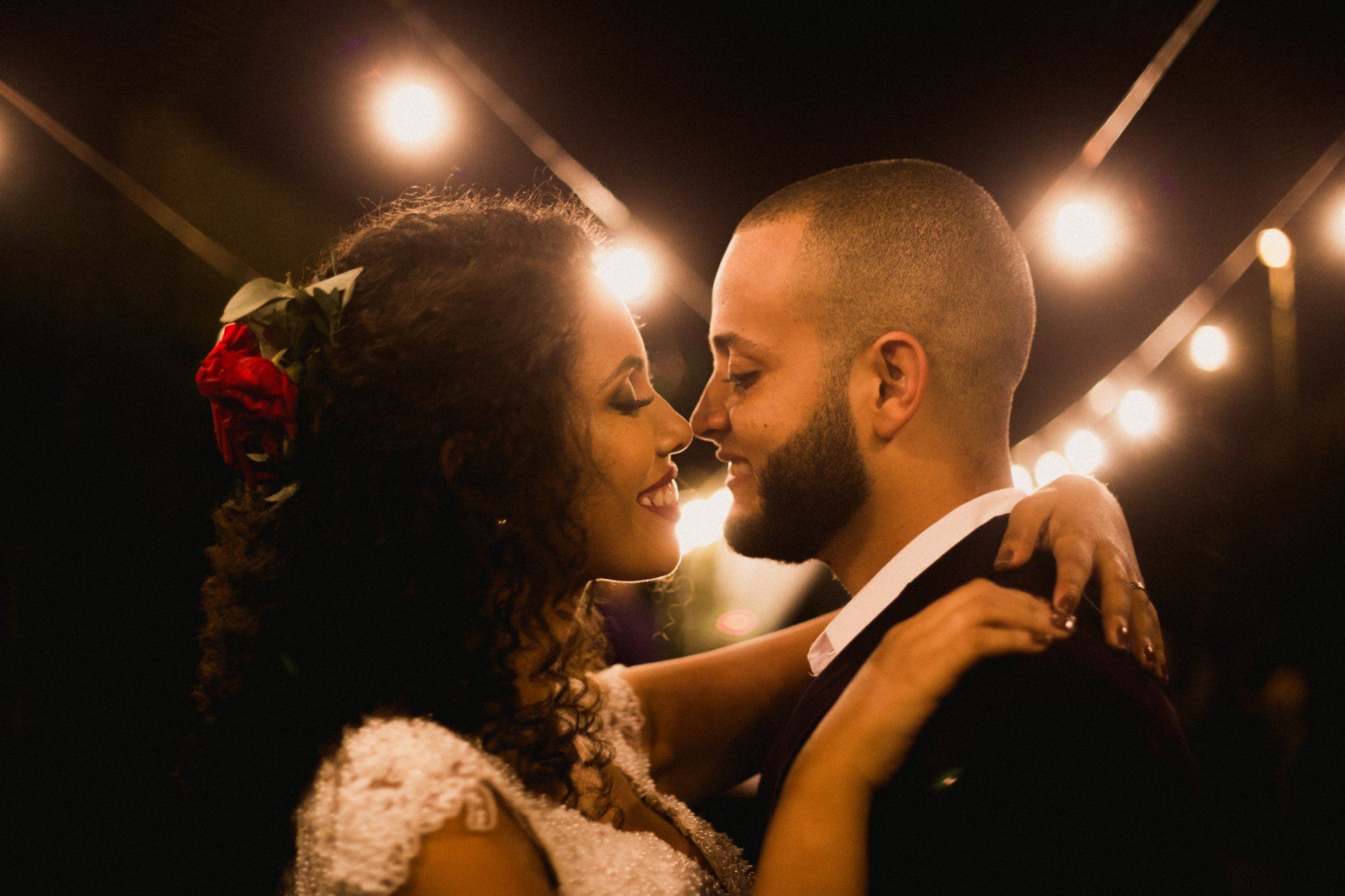 A bride and groom are dancing under a string of lights at their wedding reception.