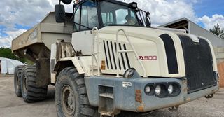 Heavy tan dump truck parked on a work site, viewed from the front-left side.