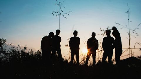 A group of people are standing in a field at sunset.