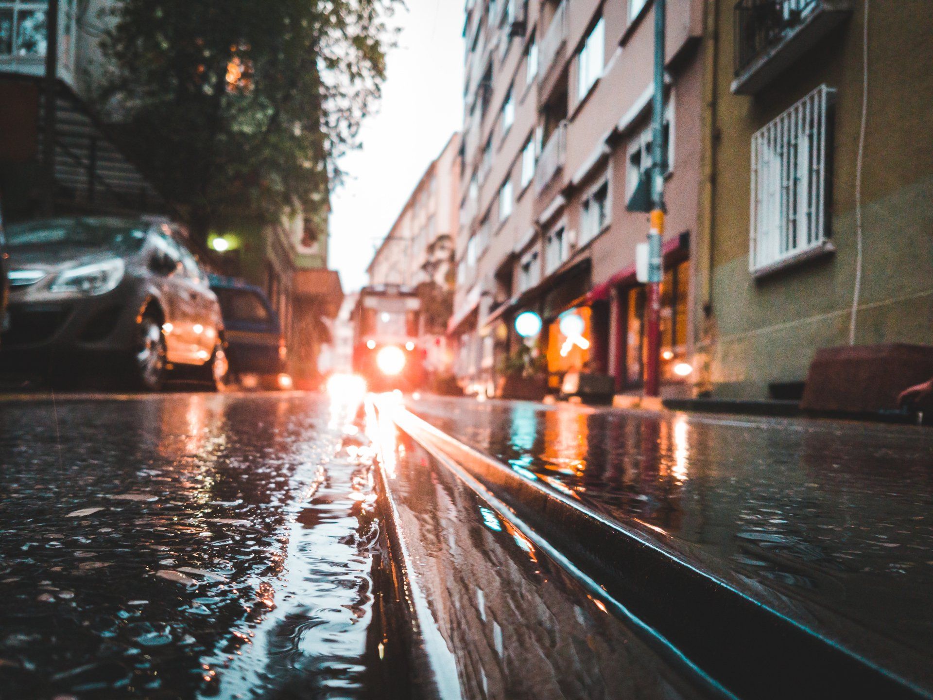 Wet city street with tram tracks reflecting lights; car and buildings in background.