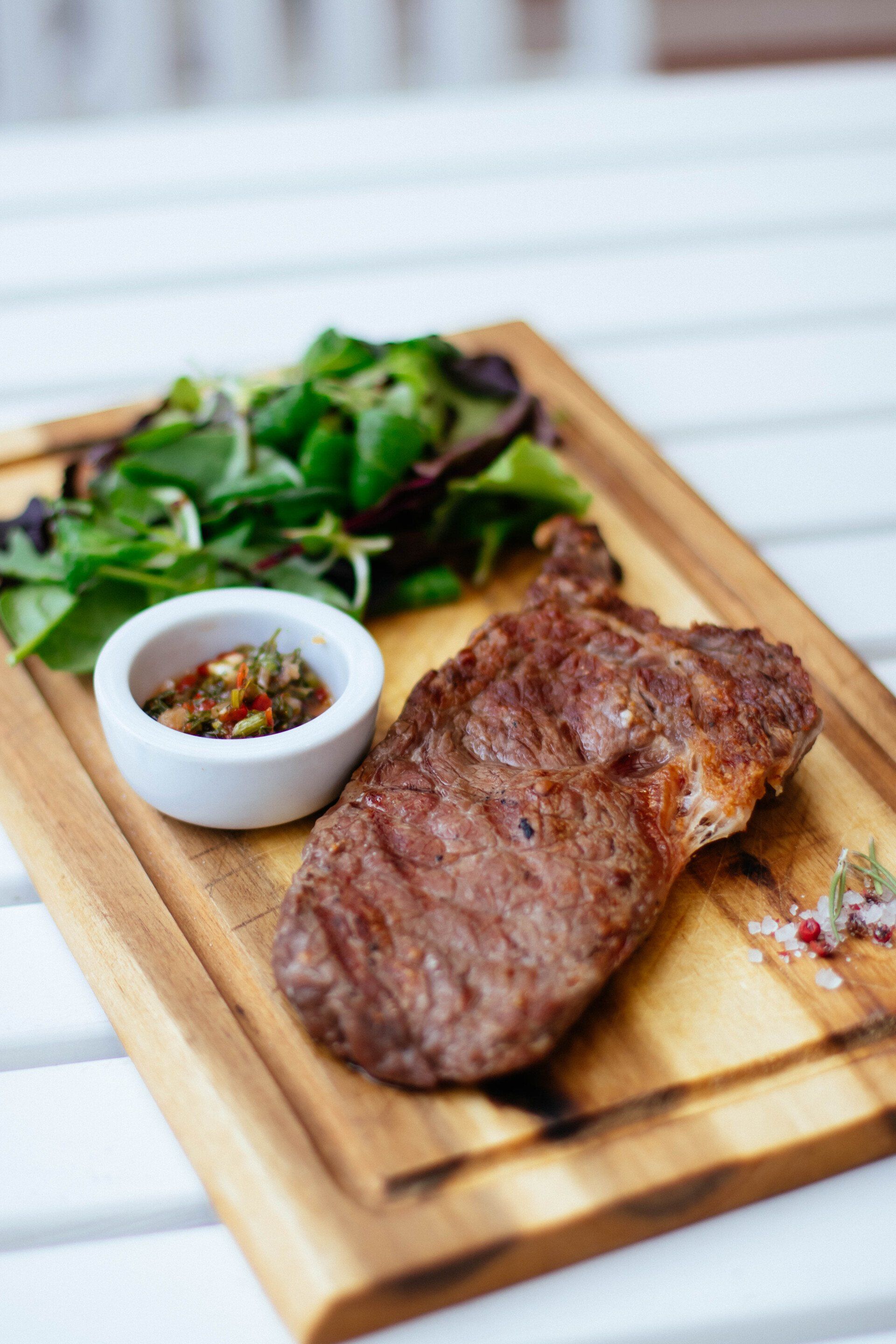 A steak and a salad on a wooden cutting board.