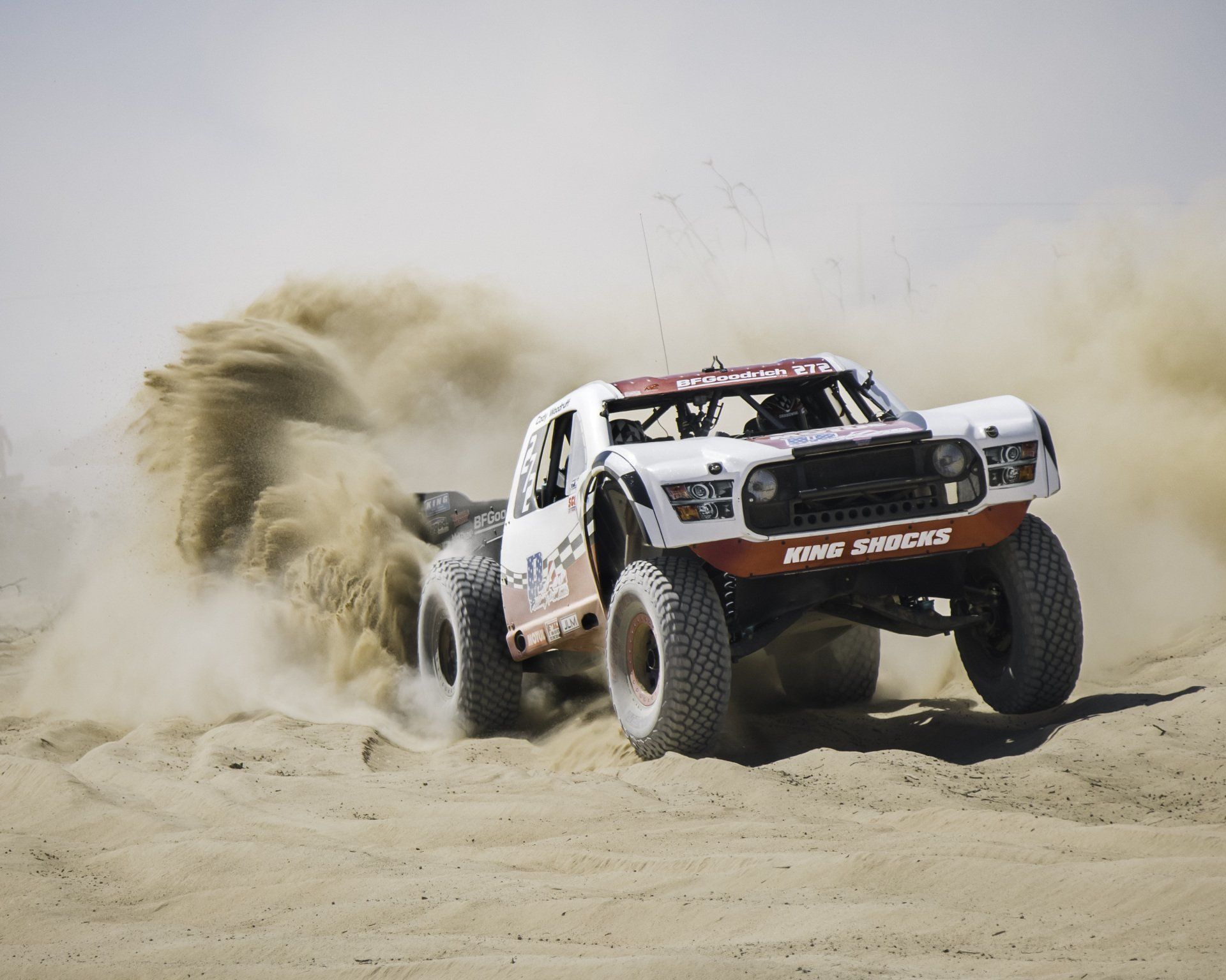 Off-road racing truck driving through sand and dust