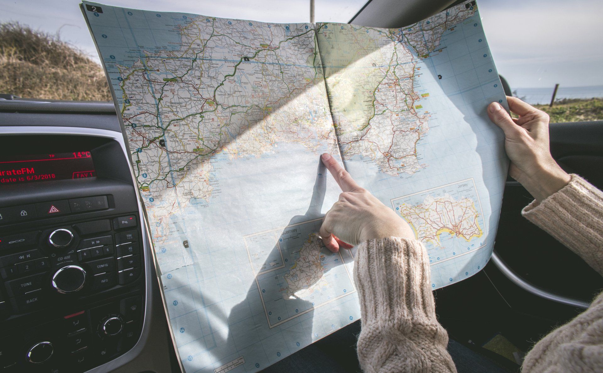 Hands holding a folded road map inside a car, with dashboard and windshield visible.