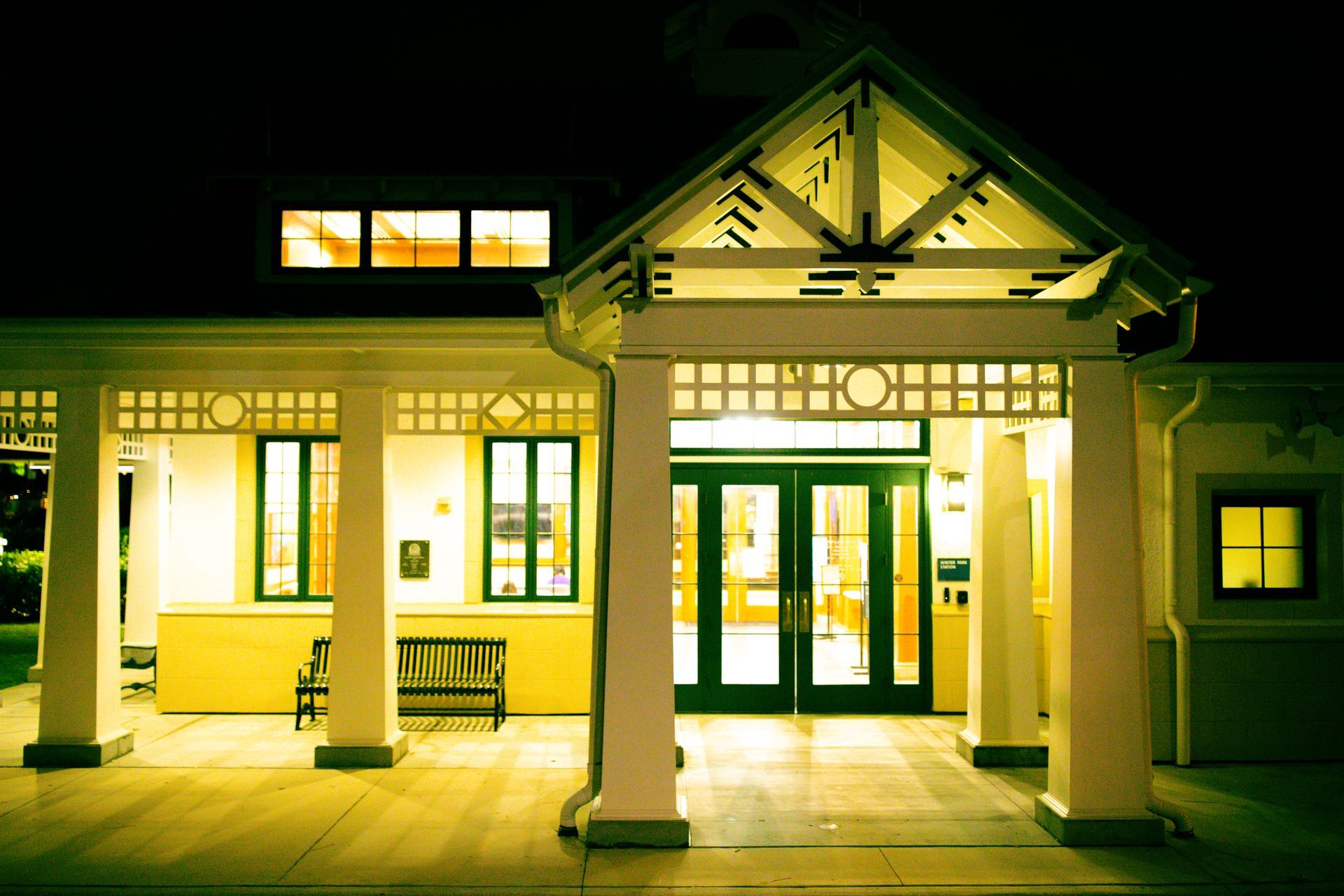 Nighttime view of a warmly lit building entrance with white columns and green doors