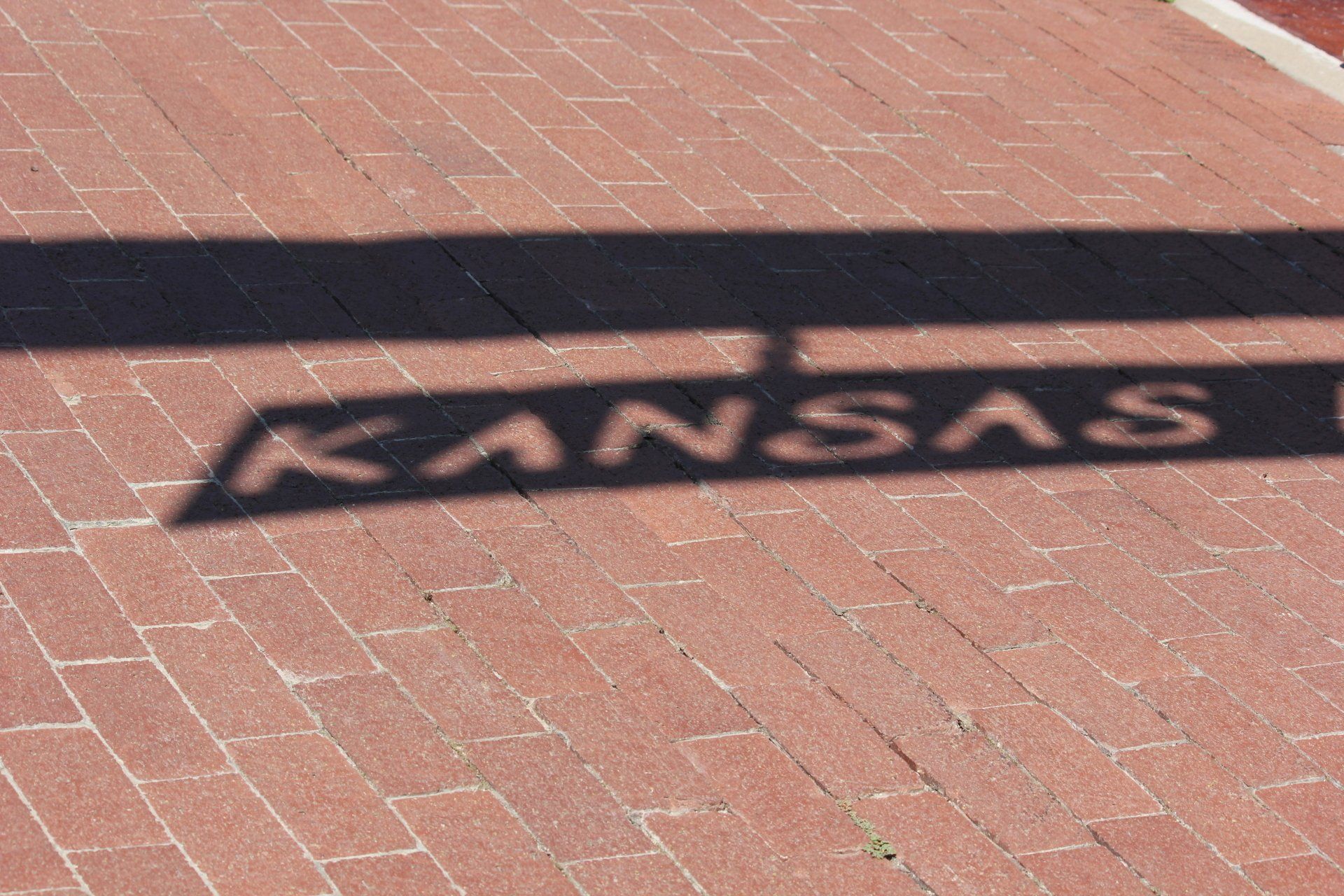 A shadow of kansas is cast on a brick sidewalk