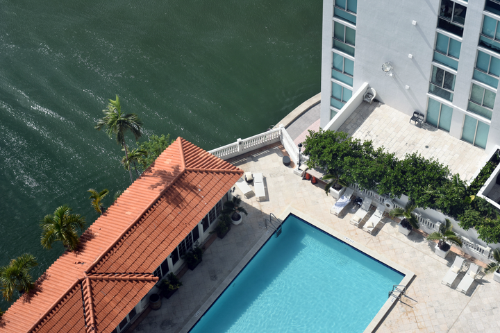 Overhead view of a building with a pool and waterfront, featuring a red tile roof and turquoise pool water.