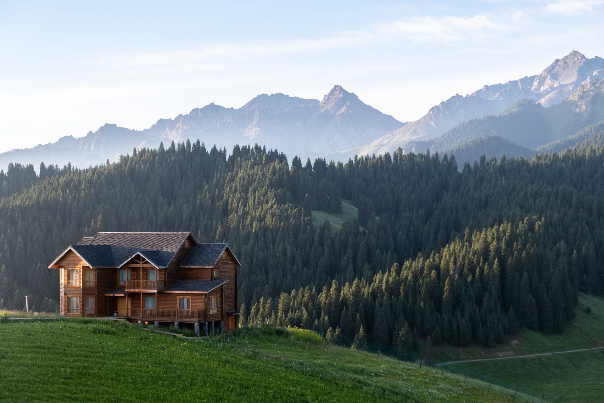 a wooden house sits on top of a grassy hill in the mountains
