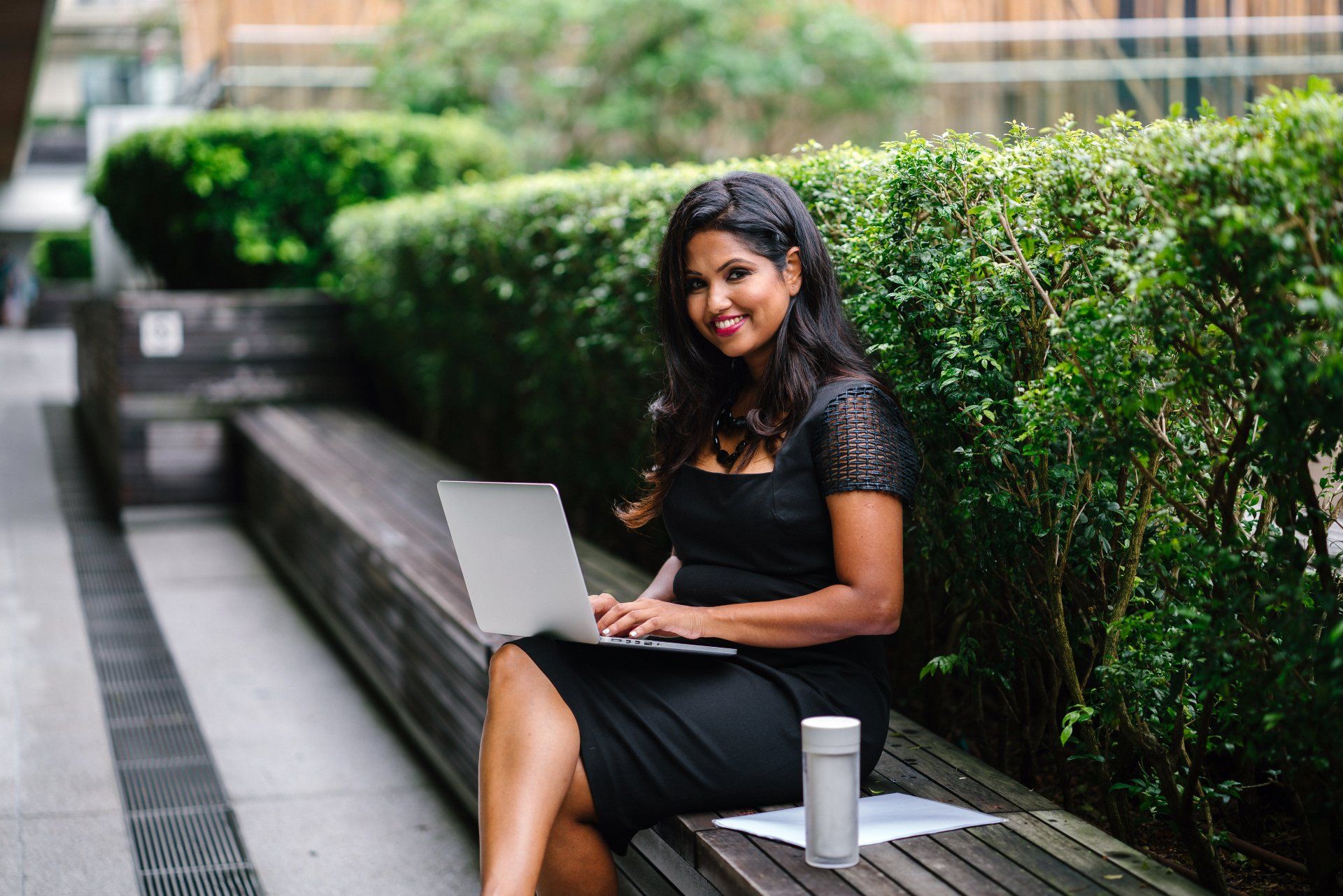A woman is sitting on a bench using a laptop computer.