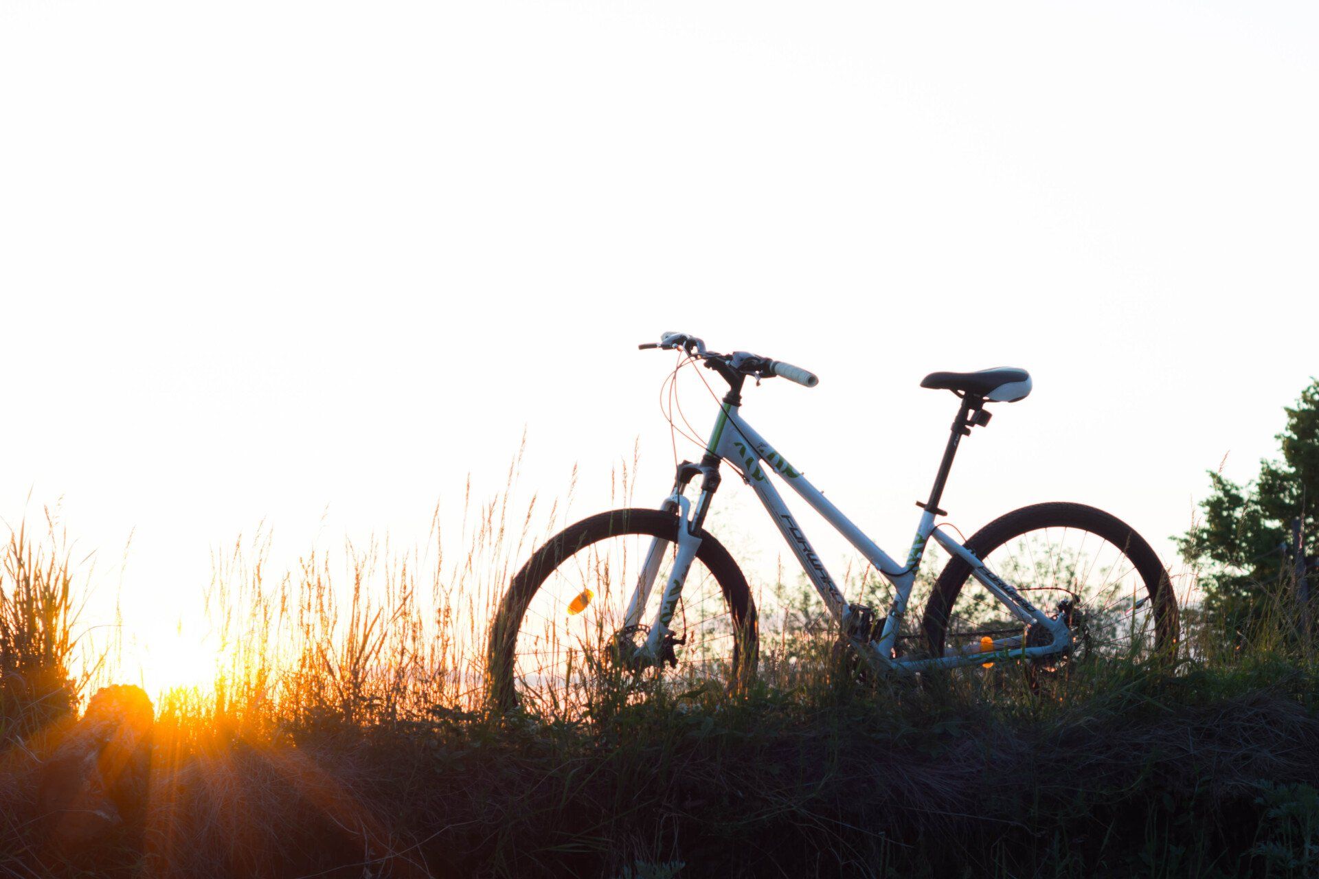 a bike in a grassy trail with he sun slowly setting over the grassy hill 