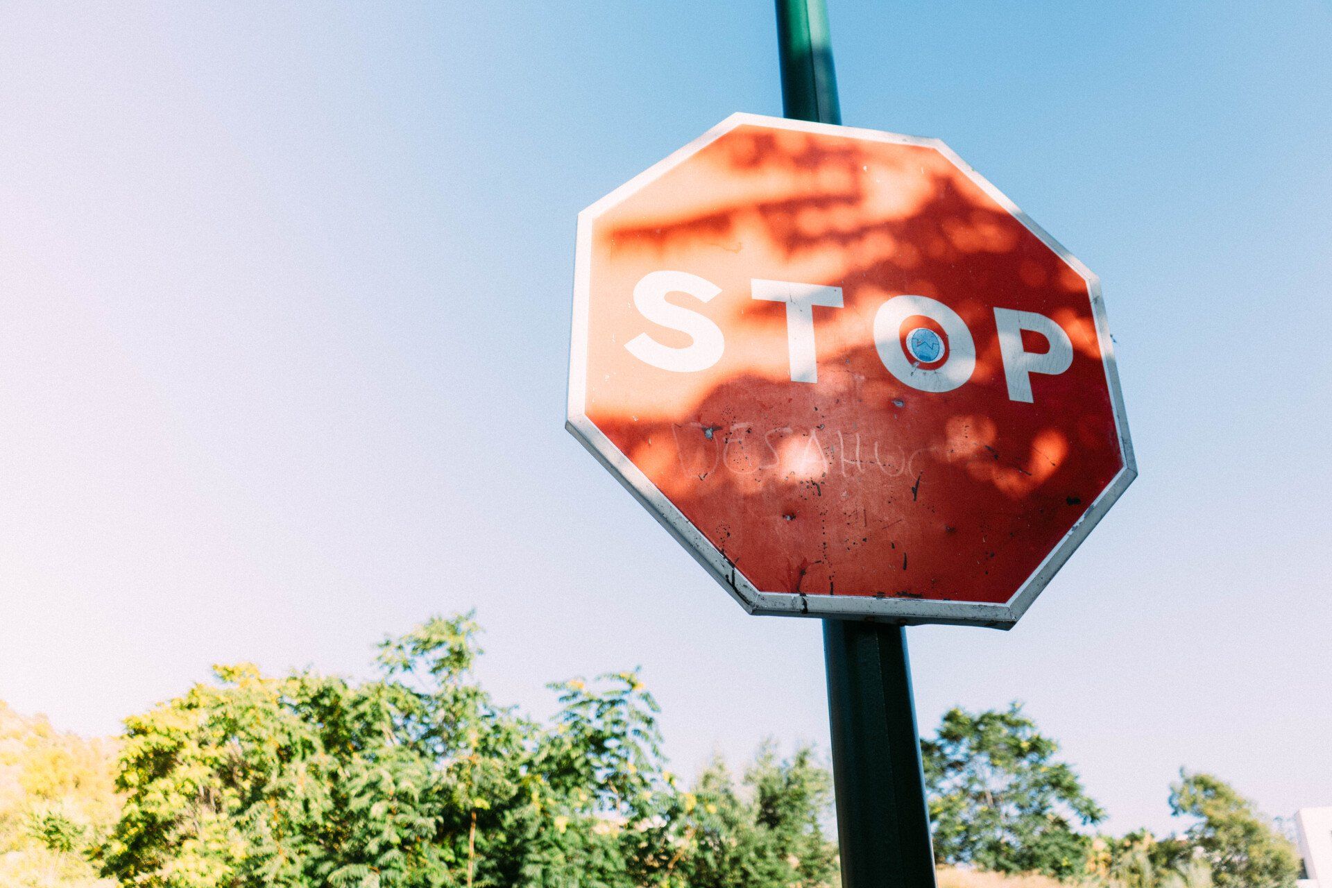 A red stop sign is sitting on top of a green pole.