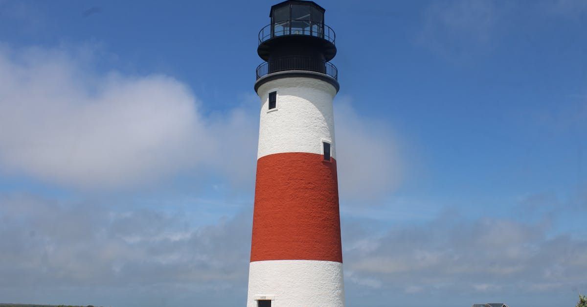 White and red striped lighthouse under a blue sky.