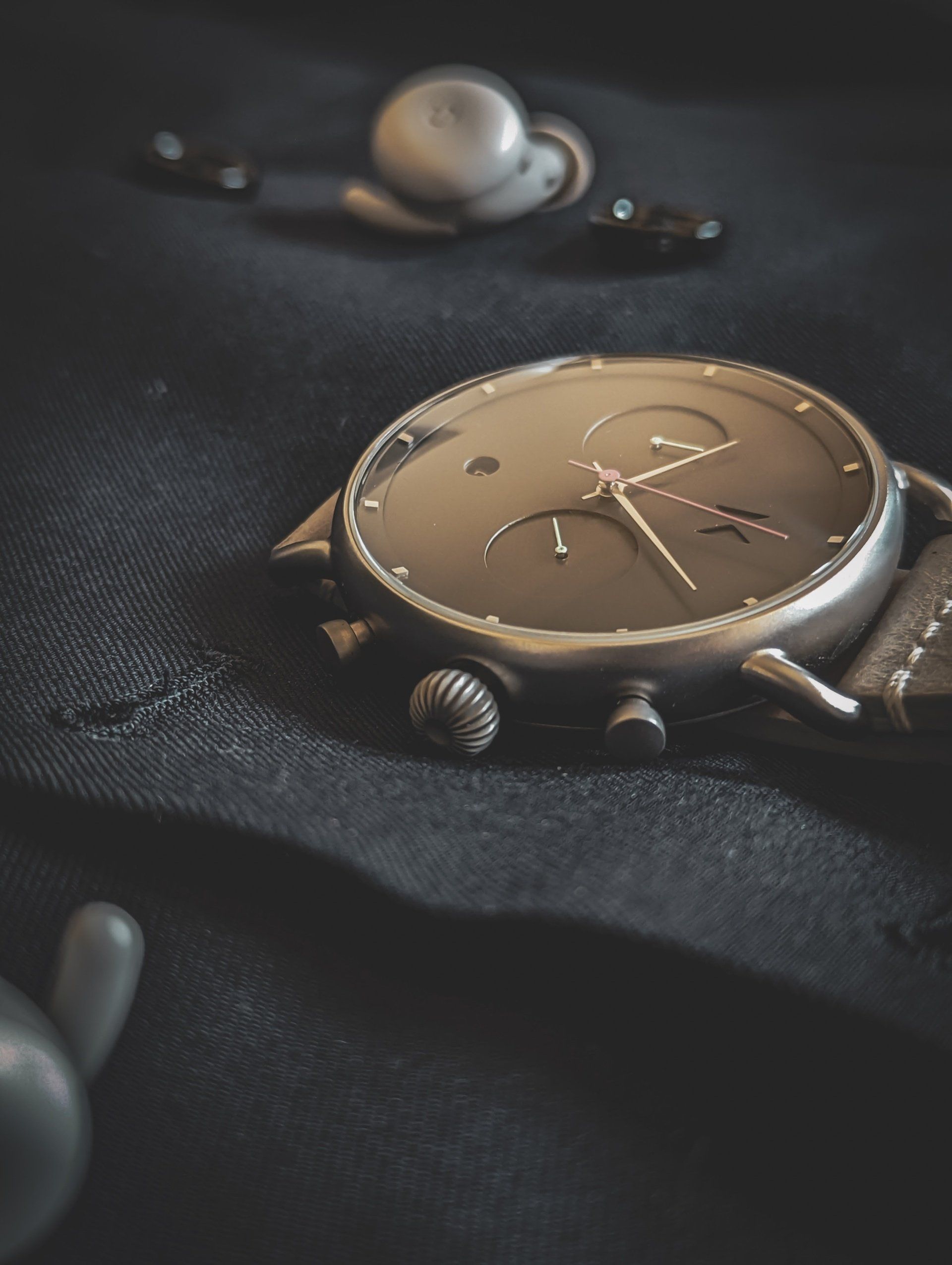 a watch is laying on a black cloth next to a pair of ear buds