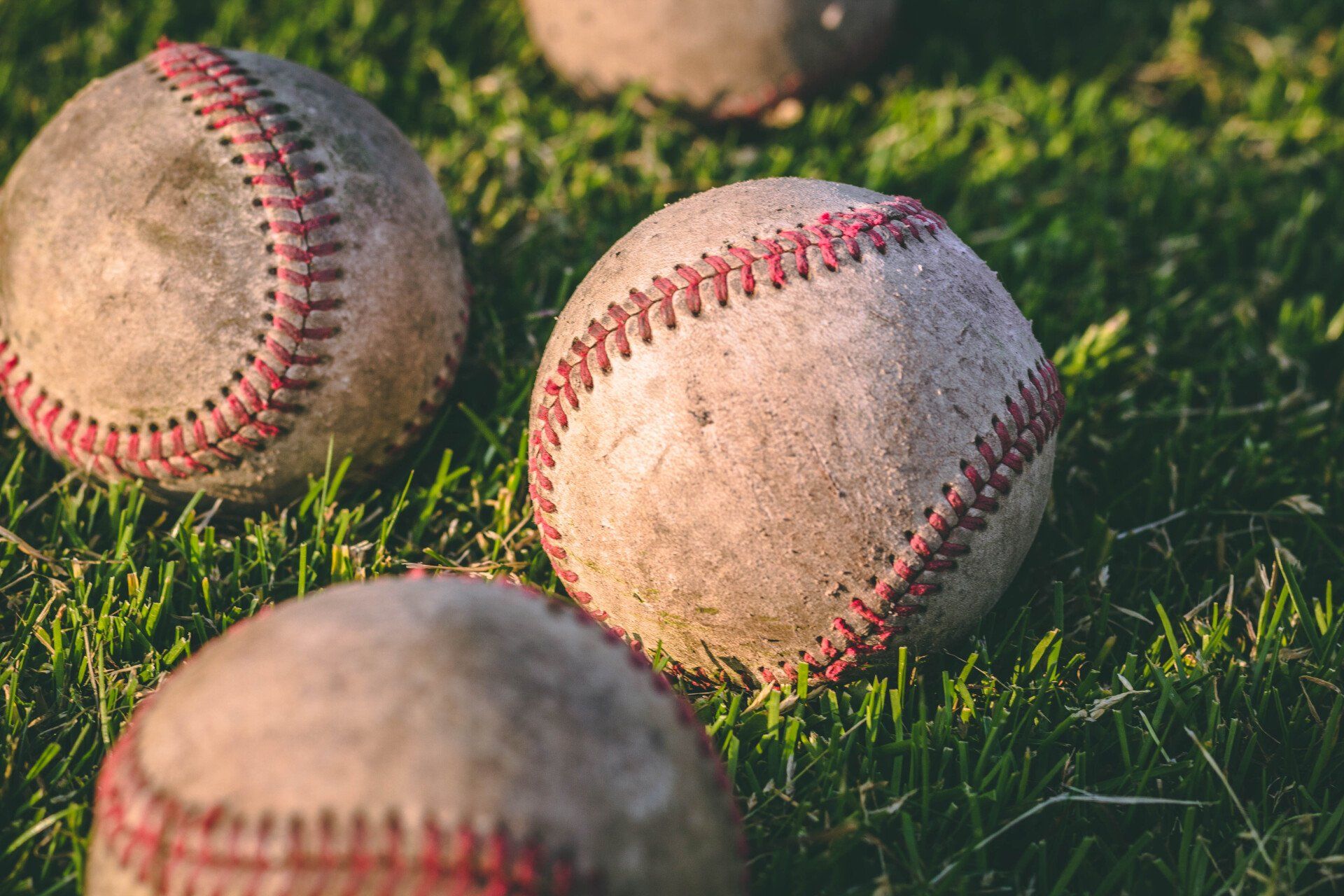 Worn baseballs resting on a green grassy field