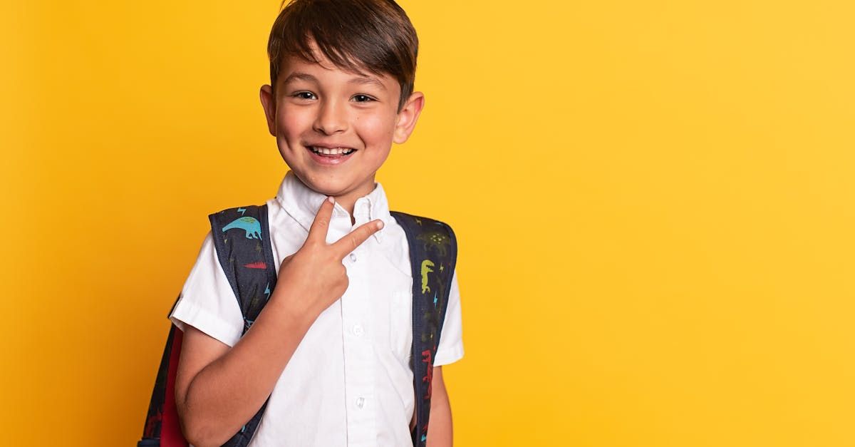 A young boy with a backpack is pointing at himself on a yellow background.