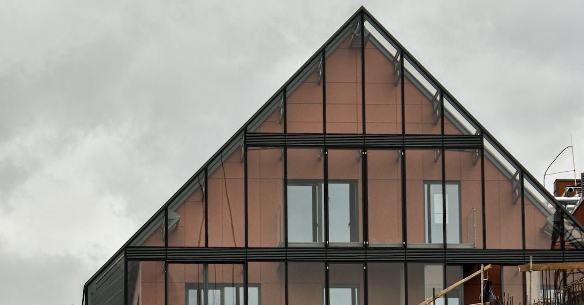 Moderne dreieckige Hausfassade mit dunklem Holzfachwerk und großen Fenstern unter einem bewölkten Himmel