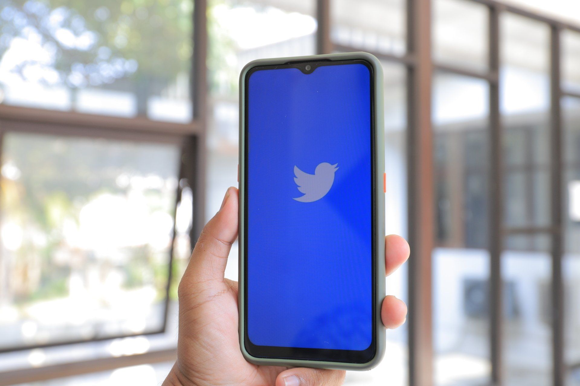 A person is holding a cell phone with a twitter logo on the screen.