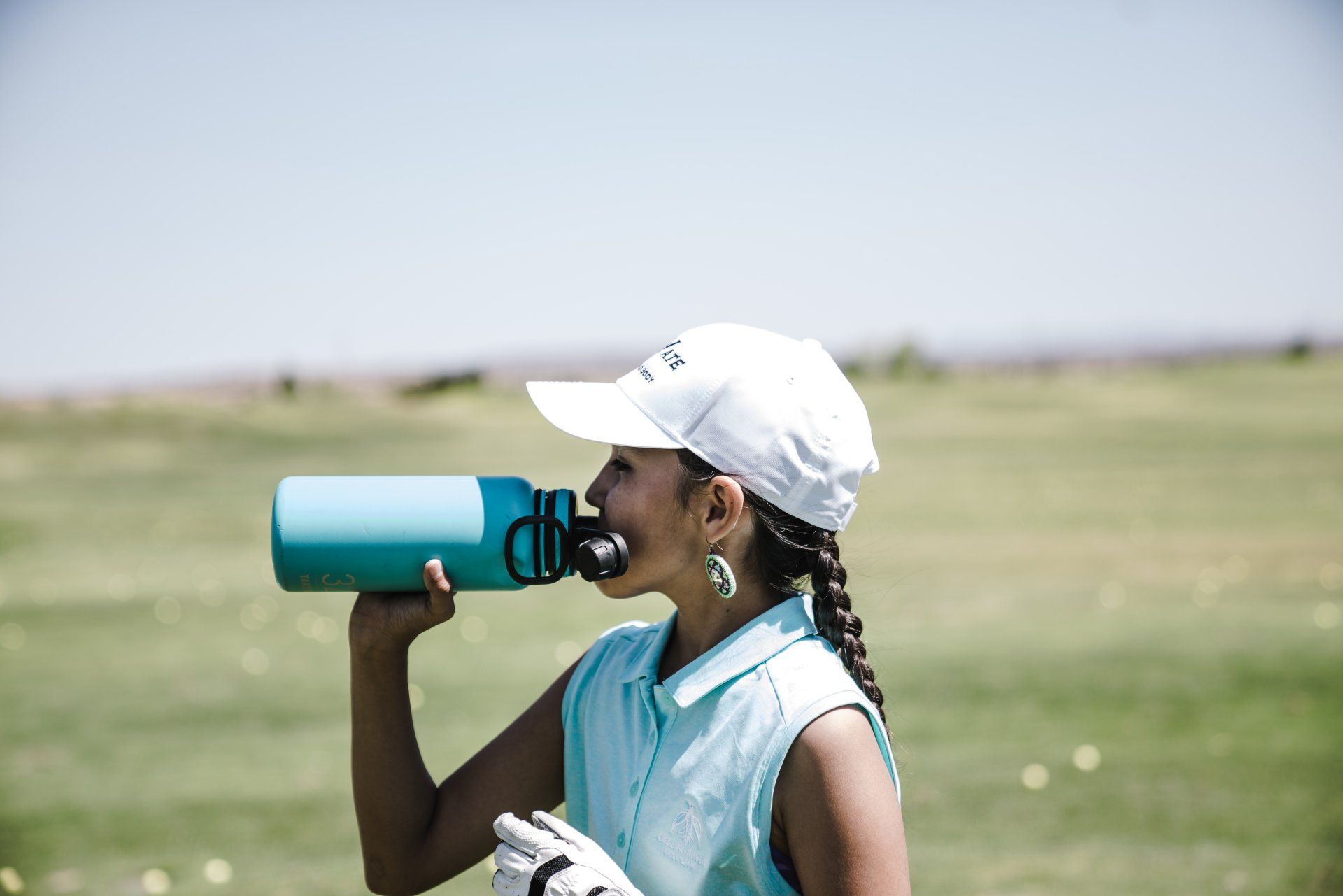 A woman is drinking water from a bottle on a golf course.