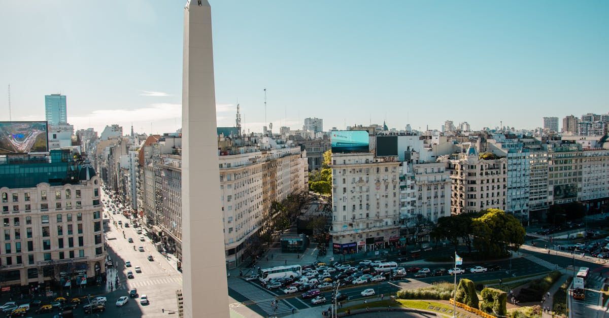 Obelisco de Buenos Aires, Argentina, frente a edificios y una calle transitada bajo un cielo azul claro.