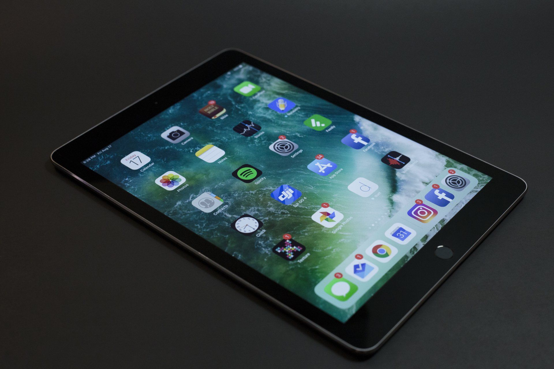 Tablet displaying app icons on a dark surface, viewed at an angle