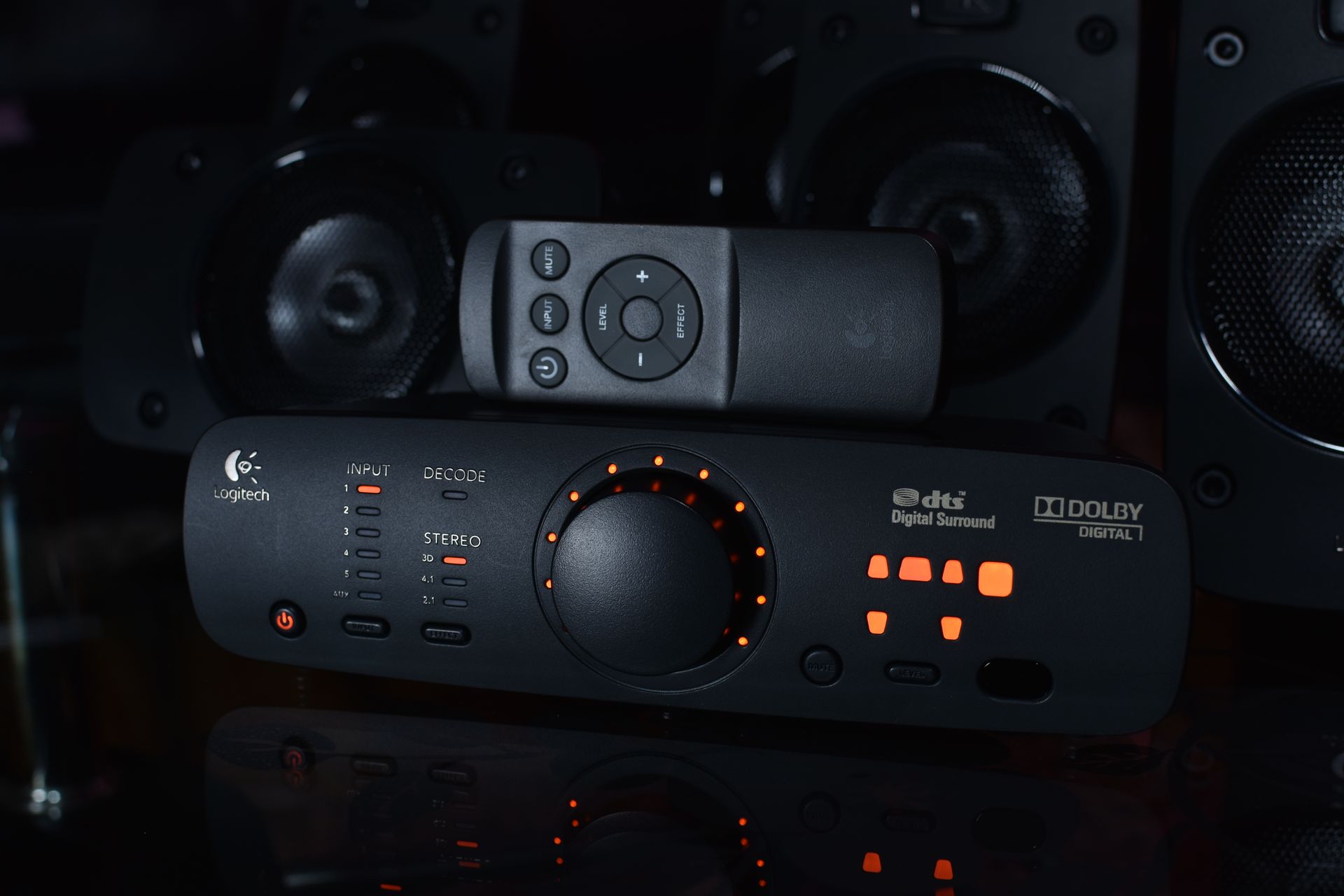 Audio receiver with glowing orange controls and a remote in front of black speakers